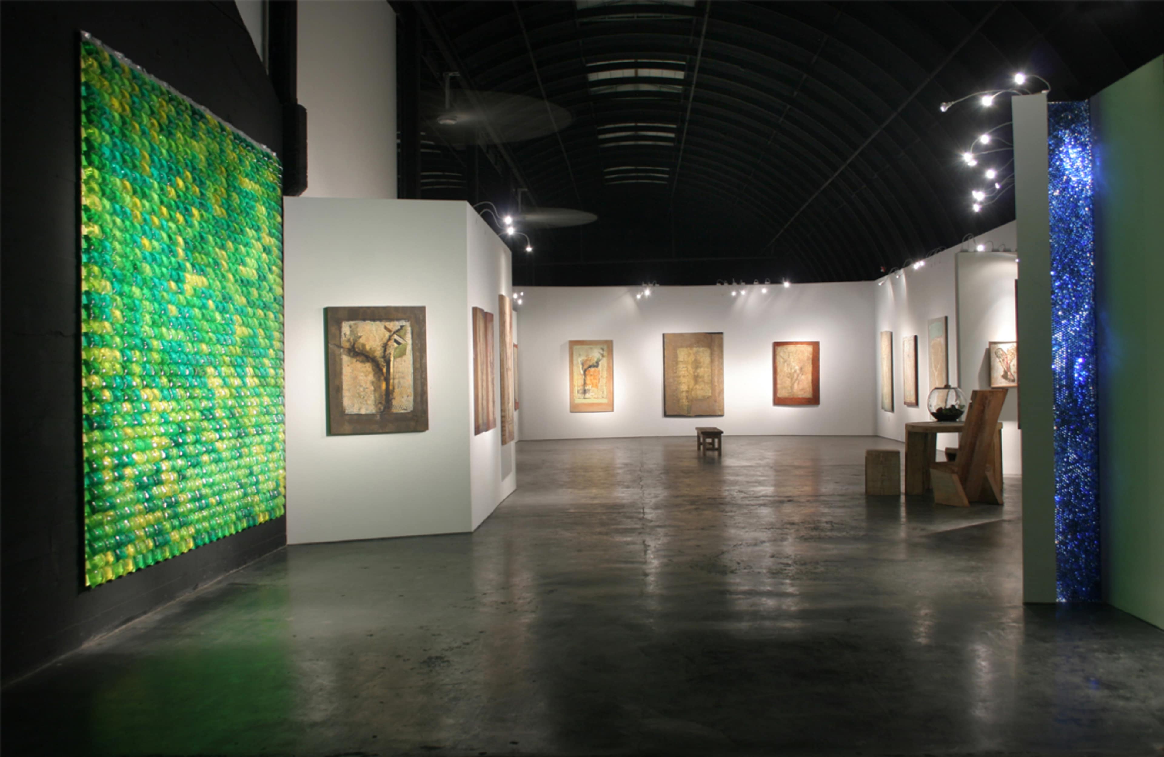 An art gallery with a green installation on the left wall and various framed artworks displayed on the white walls.