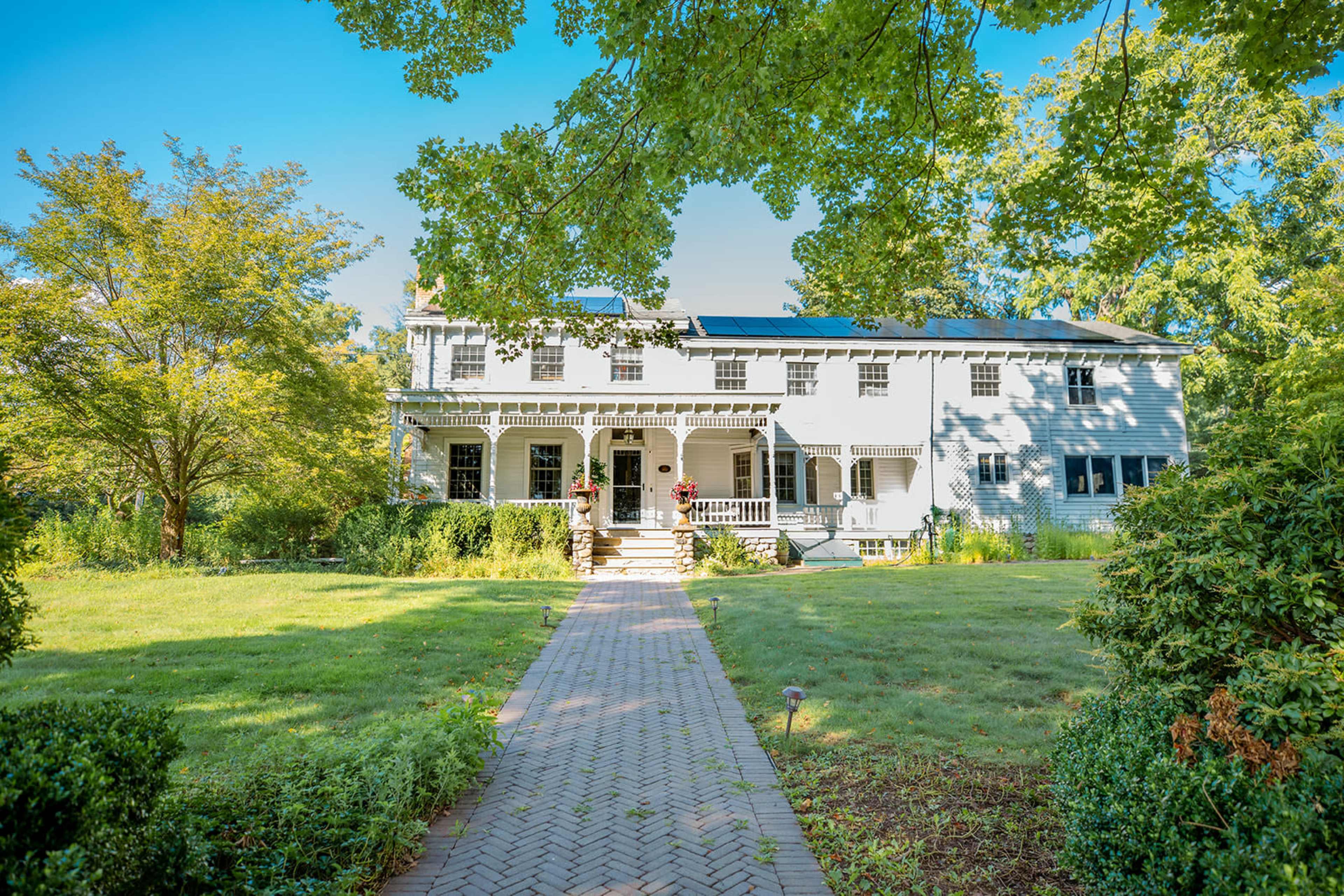 A two-story house with solar panels on the roof is set among greenery and features a walkway leading to its front entrance.