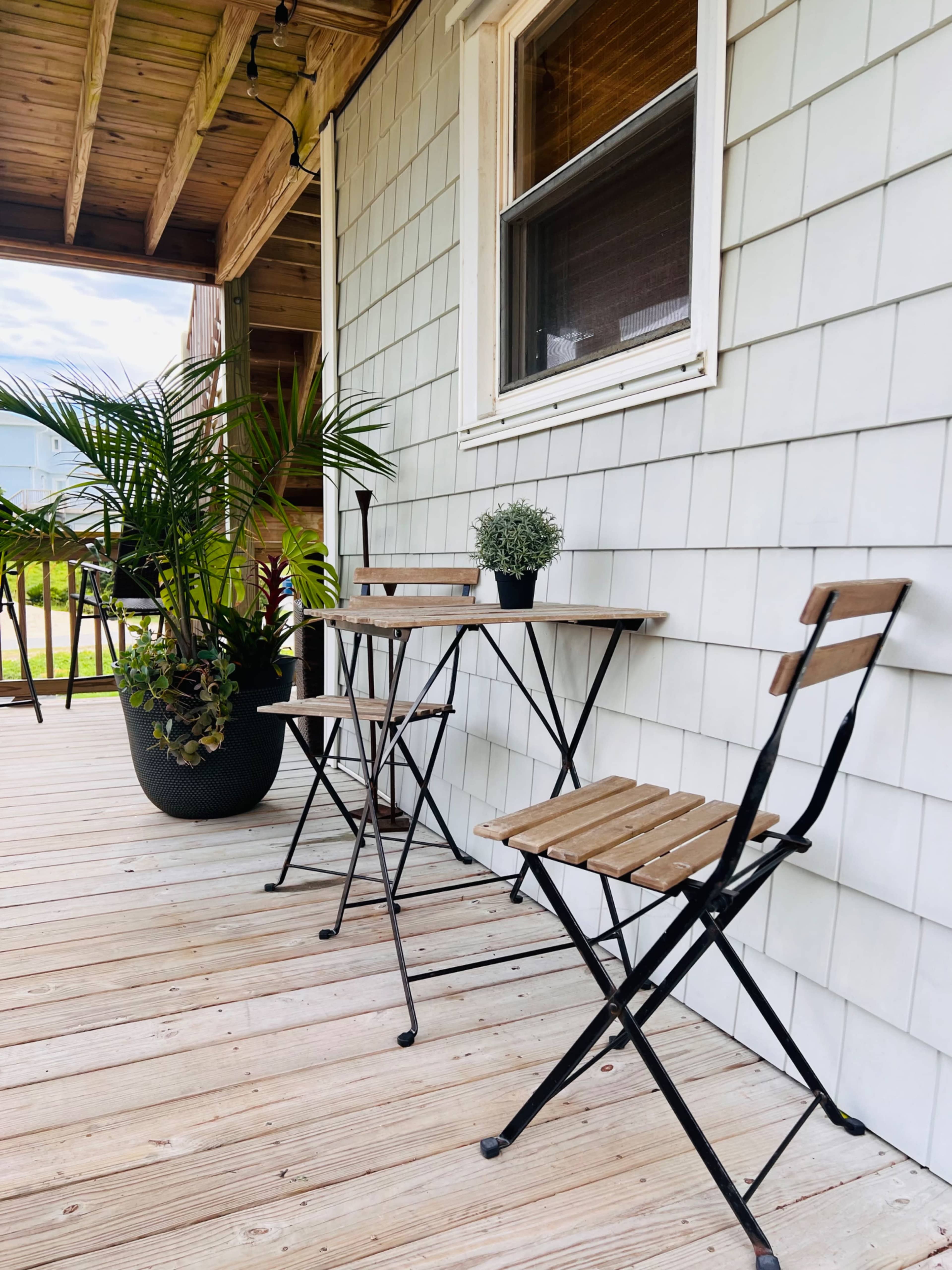 A small wooden table and two folding chairs are arranged on a porch next to potted plants.