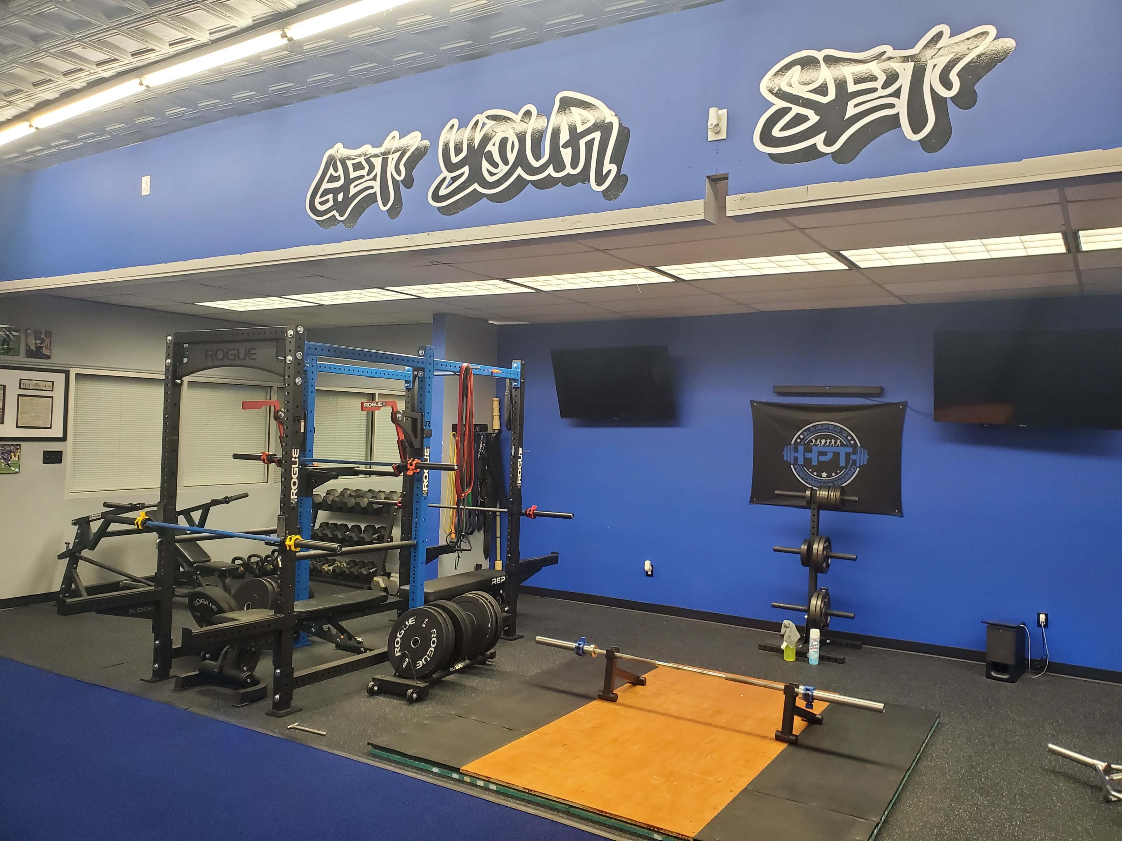 A fitness gym interior with weightlifting equipment, including a squat rack, free weights, and a weightlifting platform.