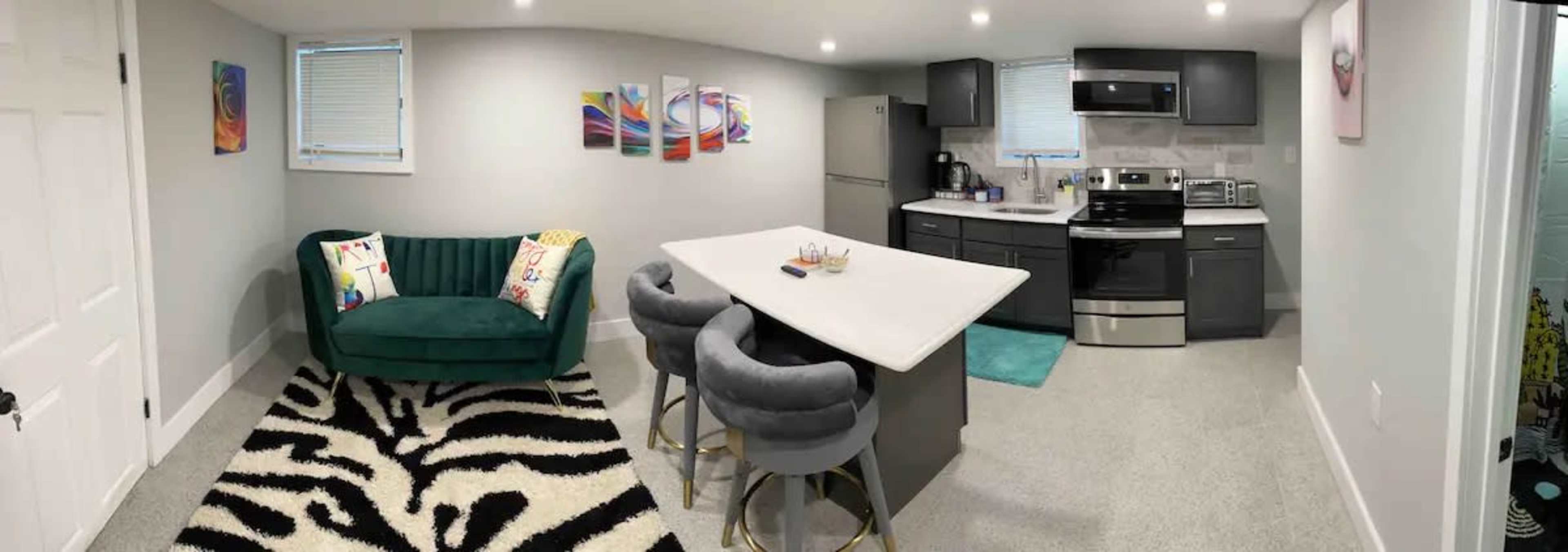 A modern kitchen and living area with a green sofa, a black and white striped rug, and sleek gray cabinetry.