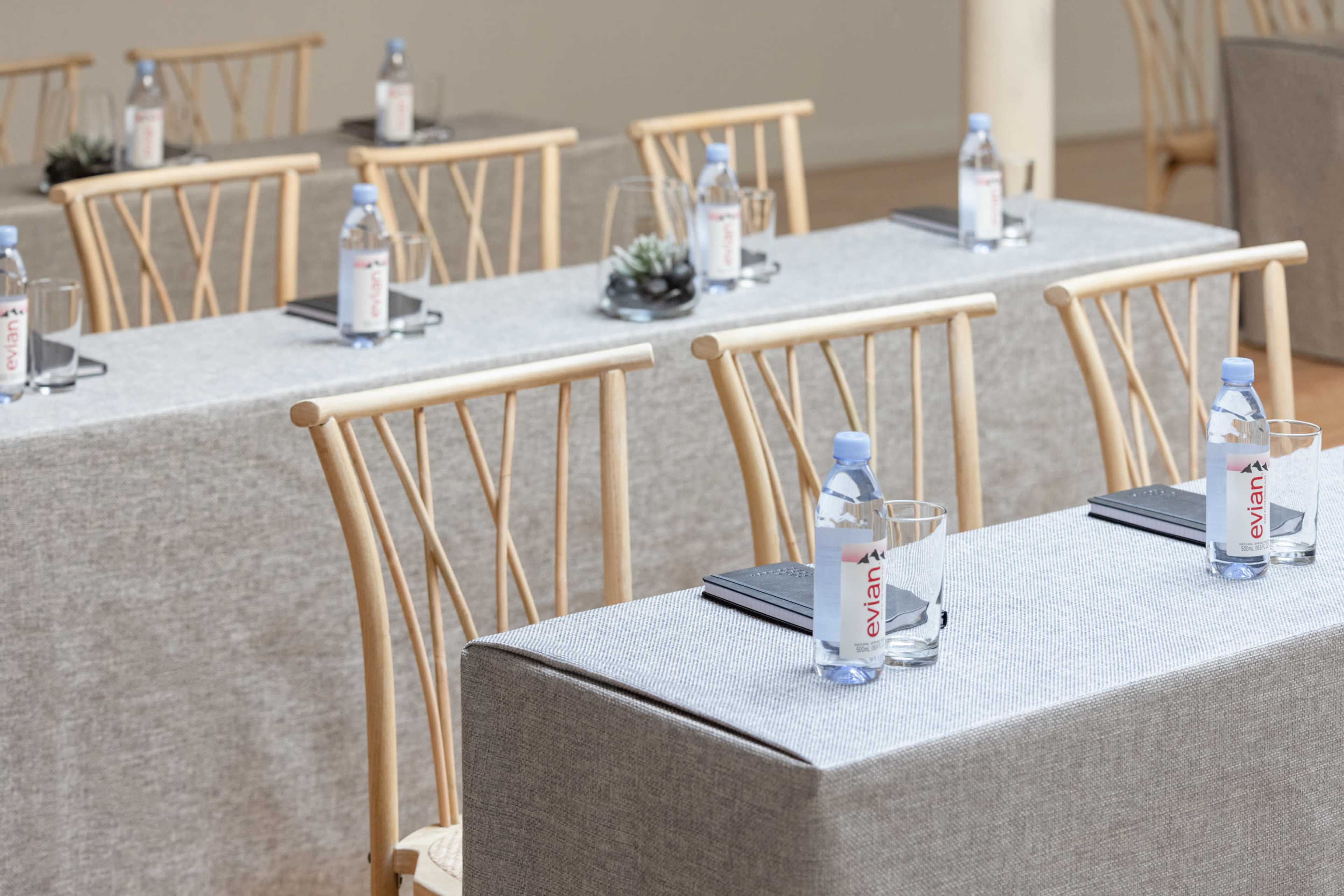 A conference setup features several tables covered in gray linen, each adorned with a bottle of Evian water, a glass, and a small plant.