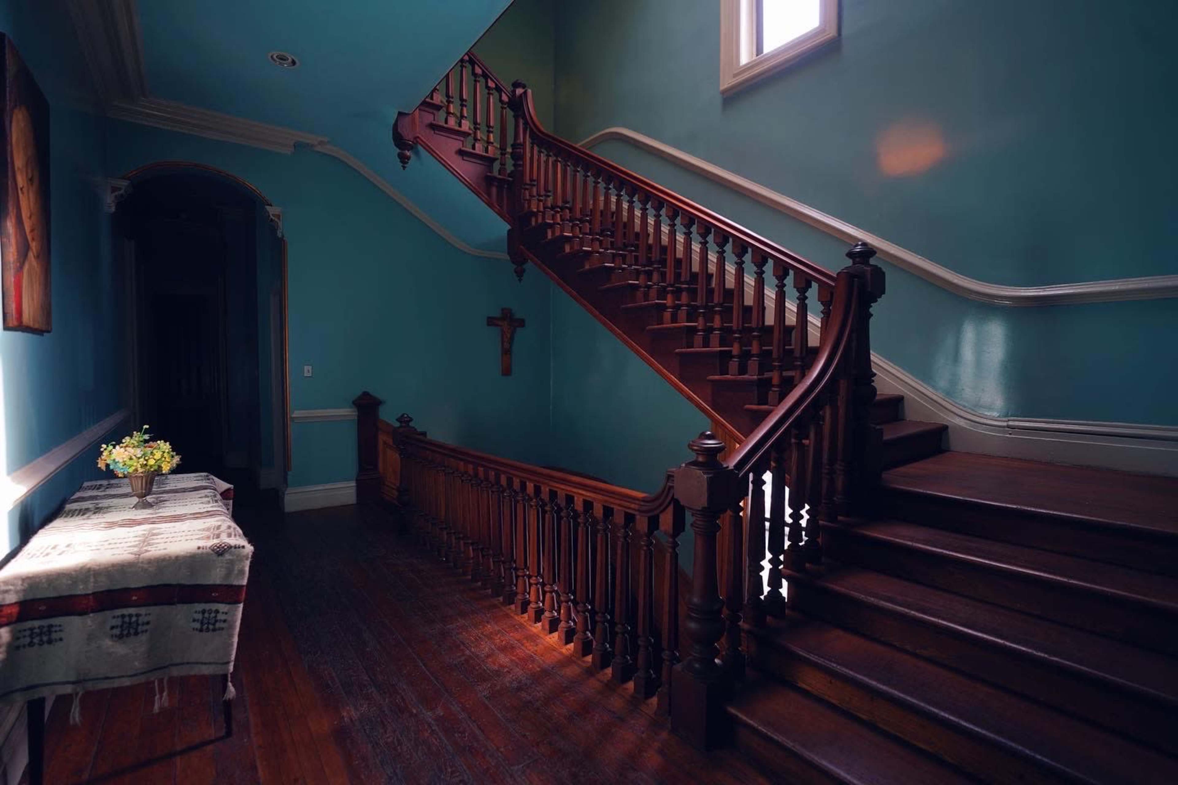 A wooden staircase with a dark banister, set against blue walls, beside a table with a floral arrangement.