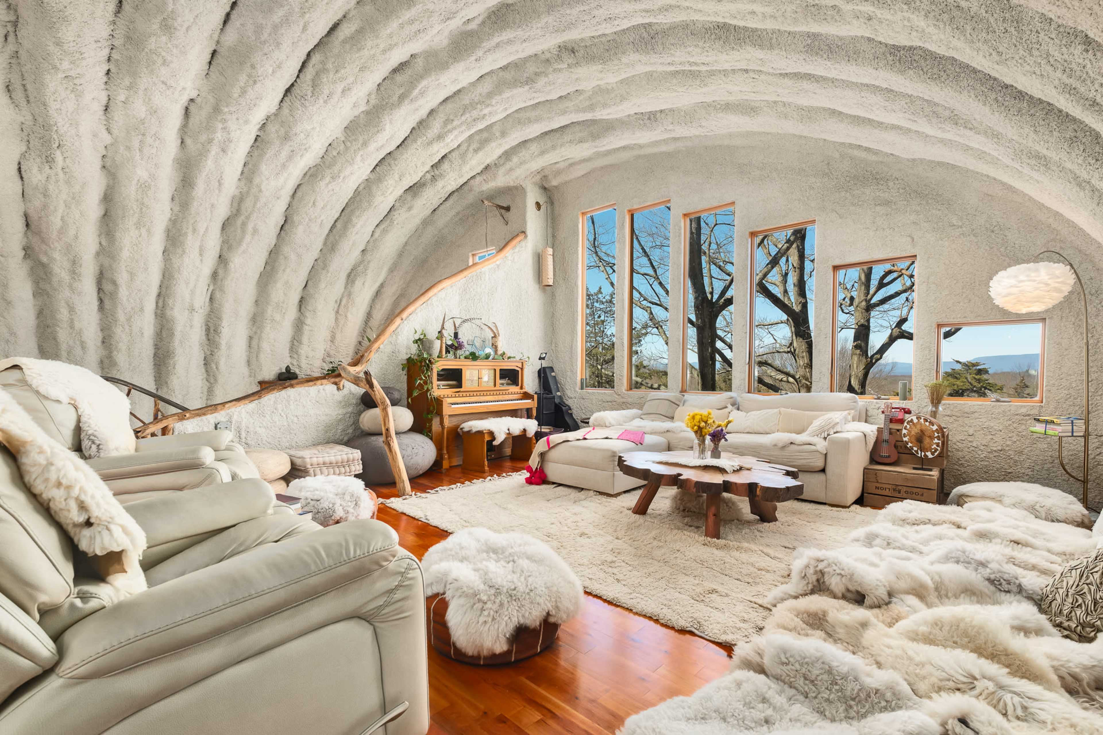 The living room features curved, textured walls, natural wood elements, and large windows overlooking a treed landscape.