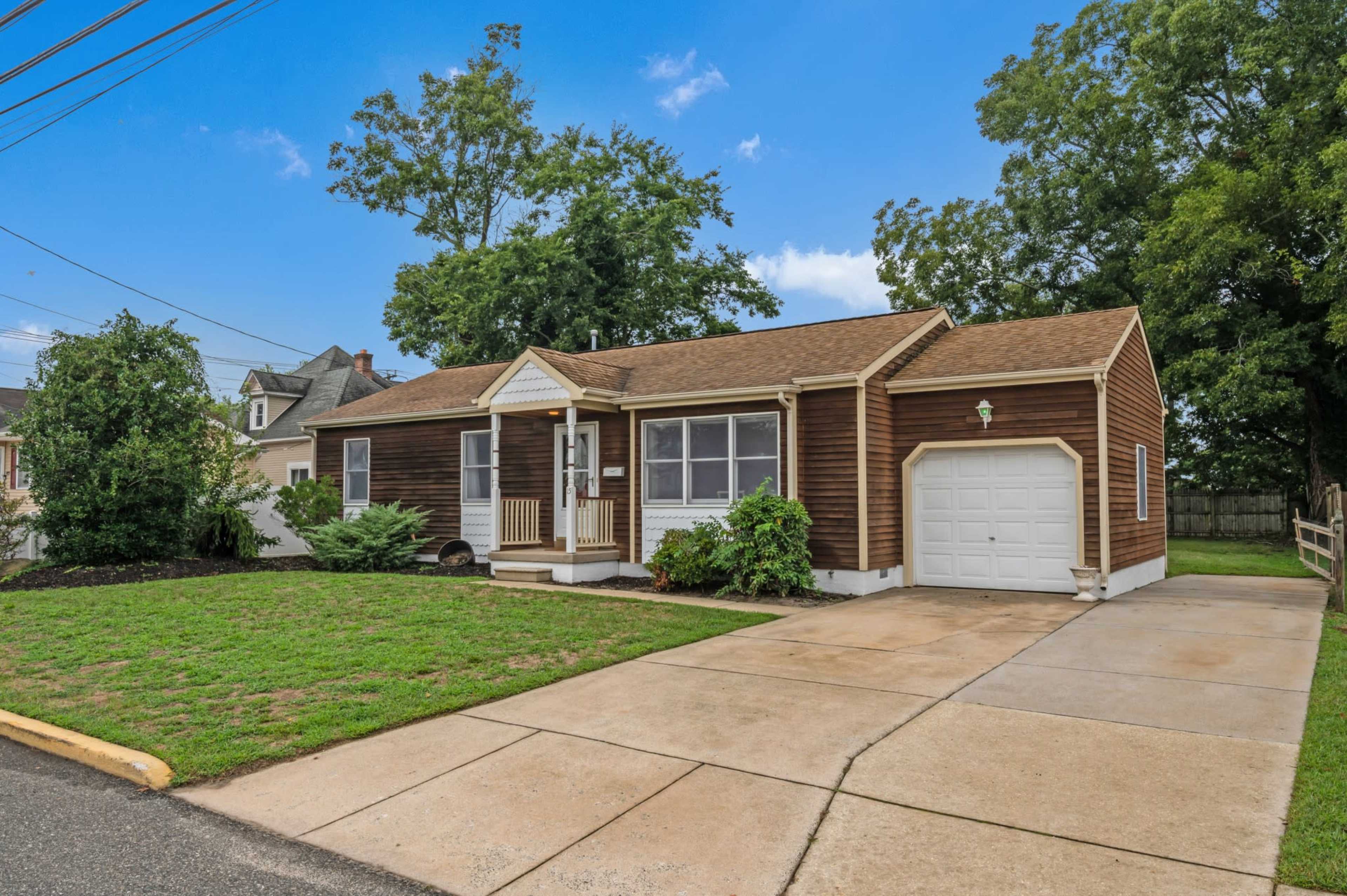 A single-story brown house with a front porch and a garage on a green lawn.