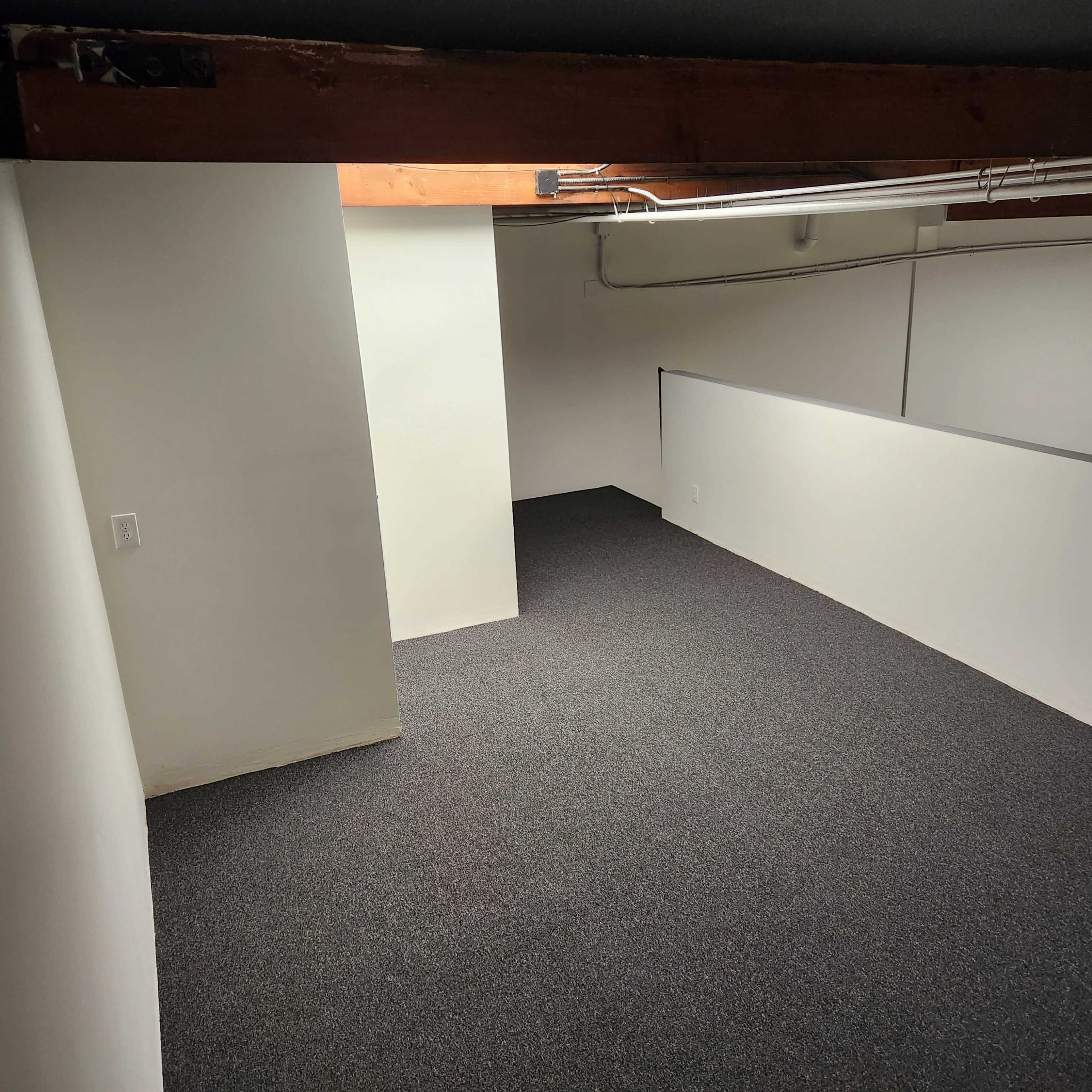 A carpeted room with white walls and a wooden beam overhead, featuring a partially enclosed area on the left.