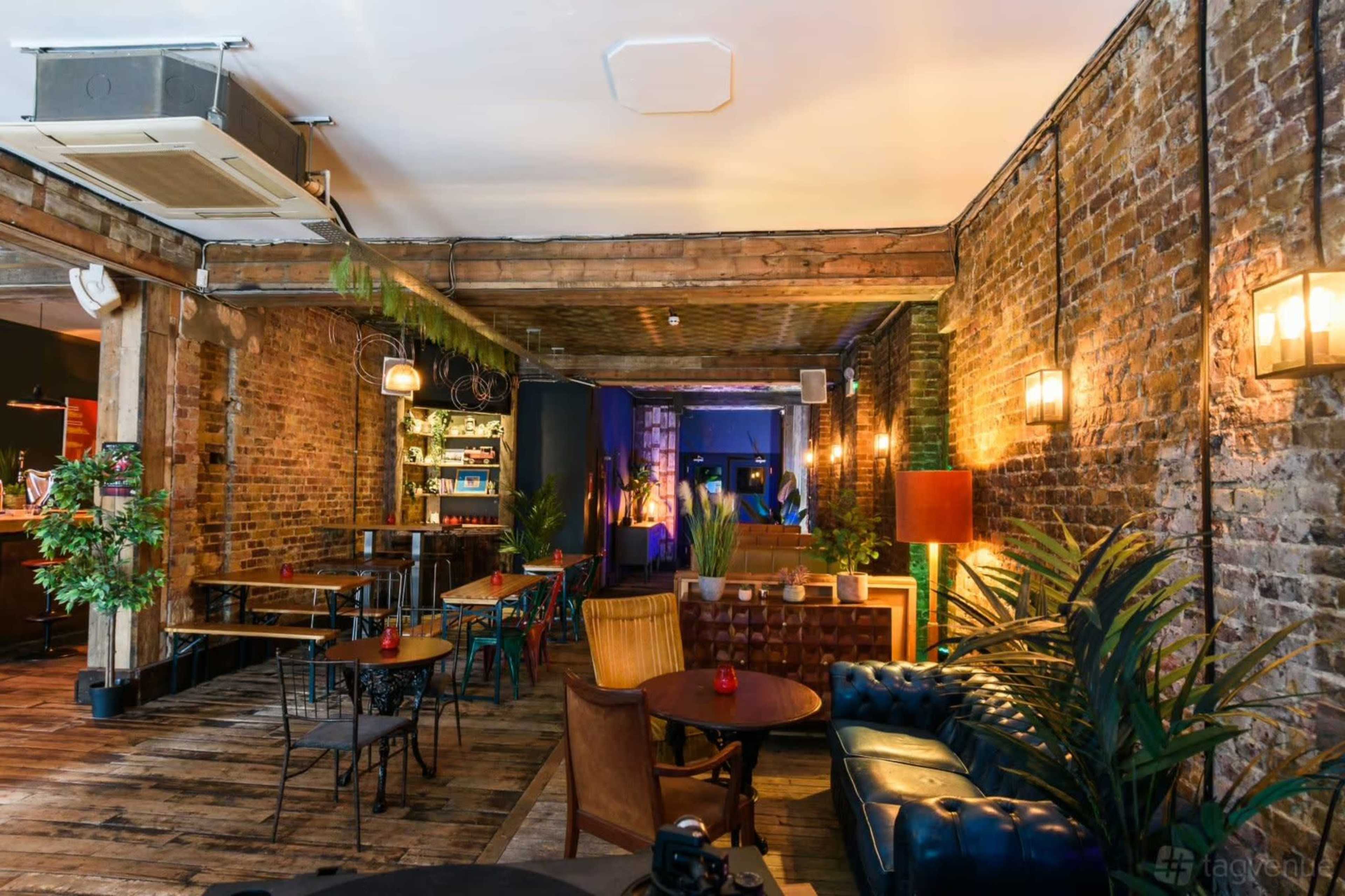 The image shows the interior of a cozy café with exposed brick walls, wooden beams, and a mix of seating arrangements, including tables and a leather couch.
