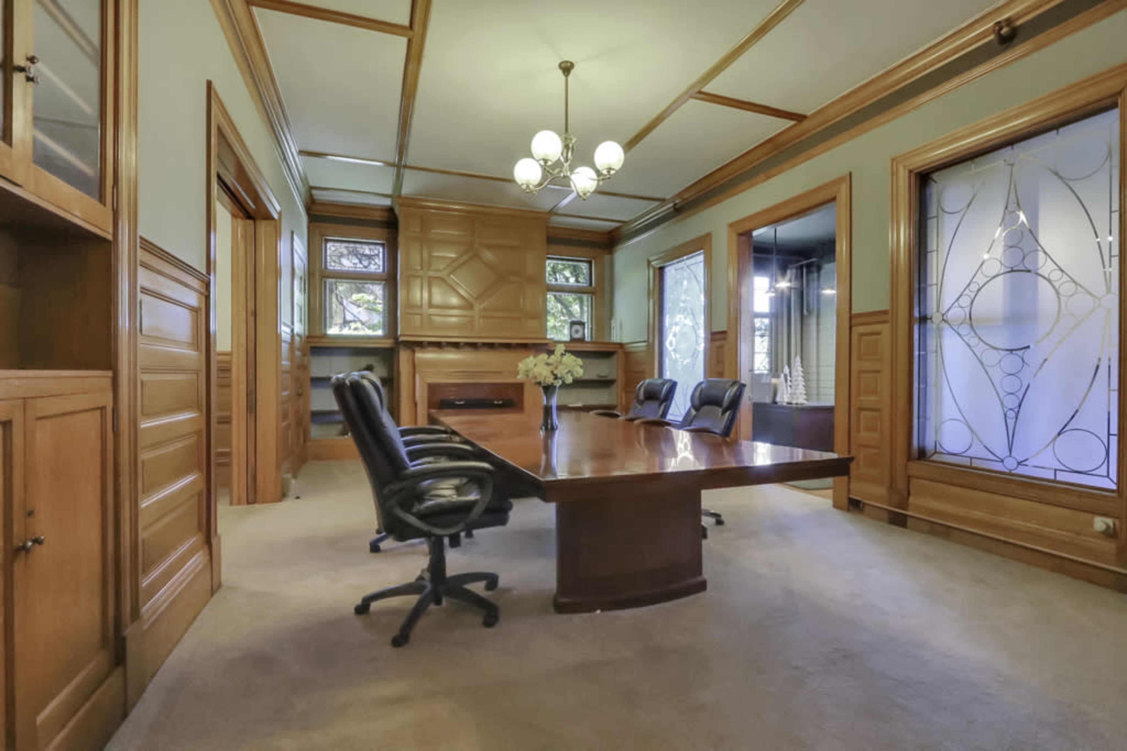A wooden conference room with a large table and several office chairs, featuring ornate paneling and decorative windows.