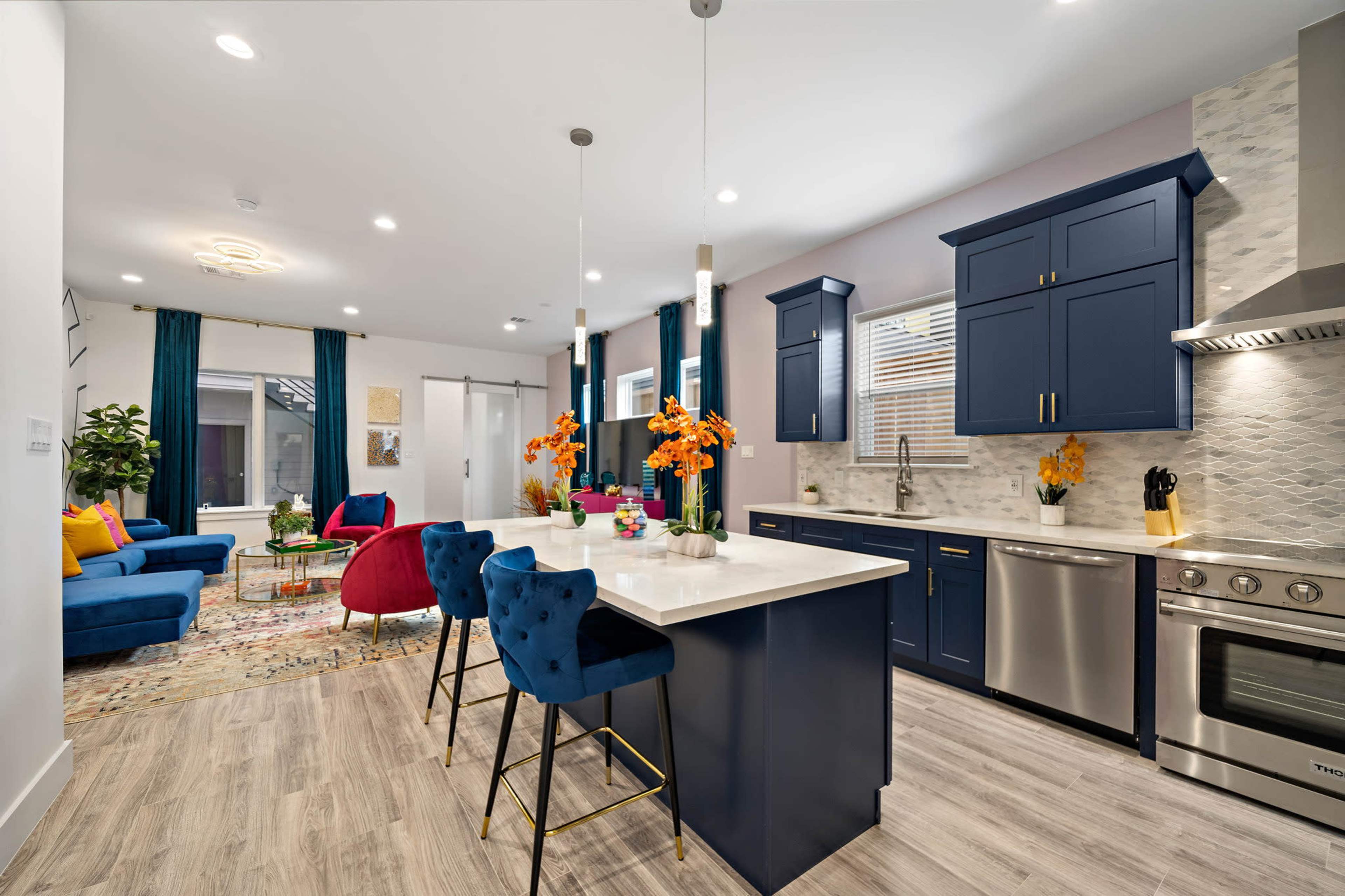 A modern kitchen and living area with navy blue cabinetry, a bright island with bar stools, and colorful furnishings.