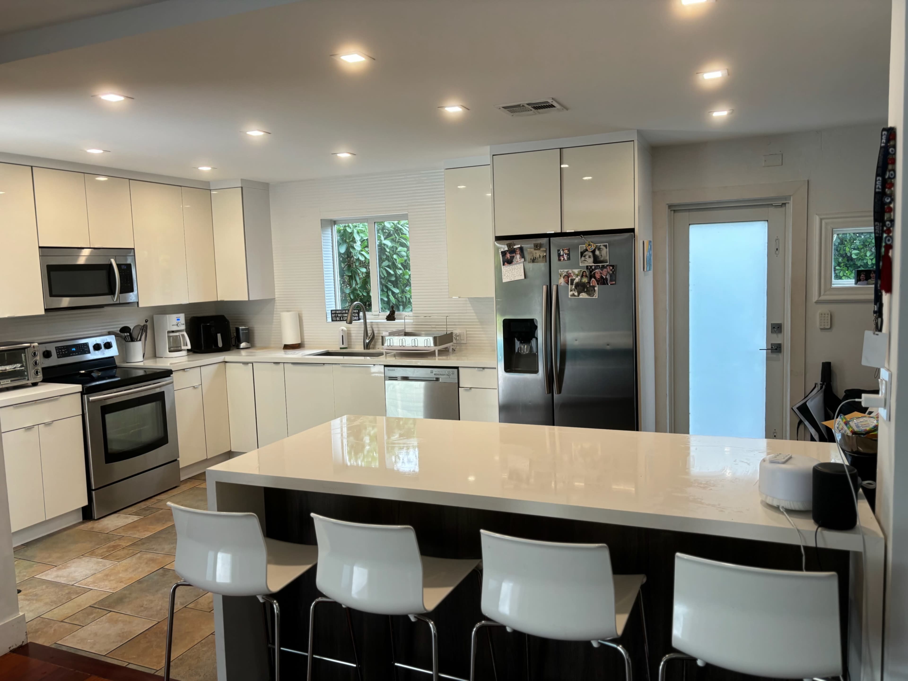 A modern kitchen features white cabinetry, stainless steel appliances, and a central island with four barstools.