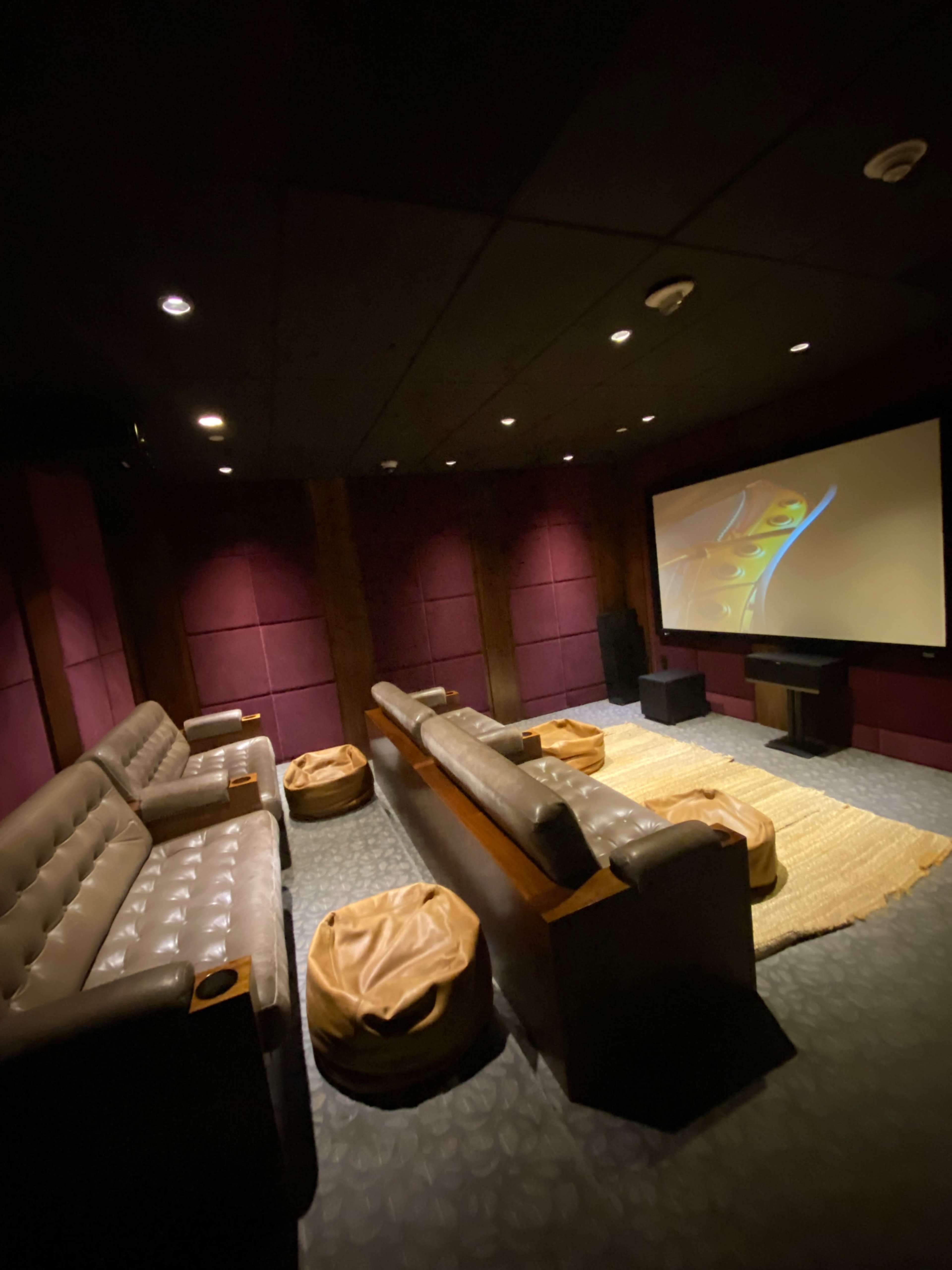 The image shows a dimly lit home theater with leather seating, bean bag chairs, and a large screen at the front.