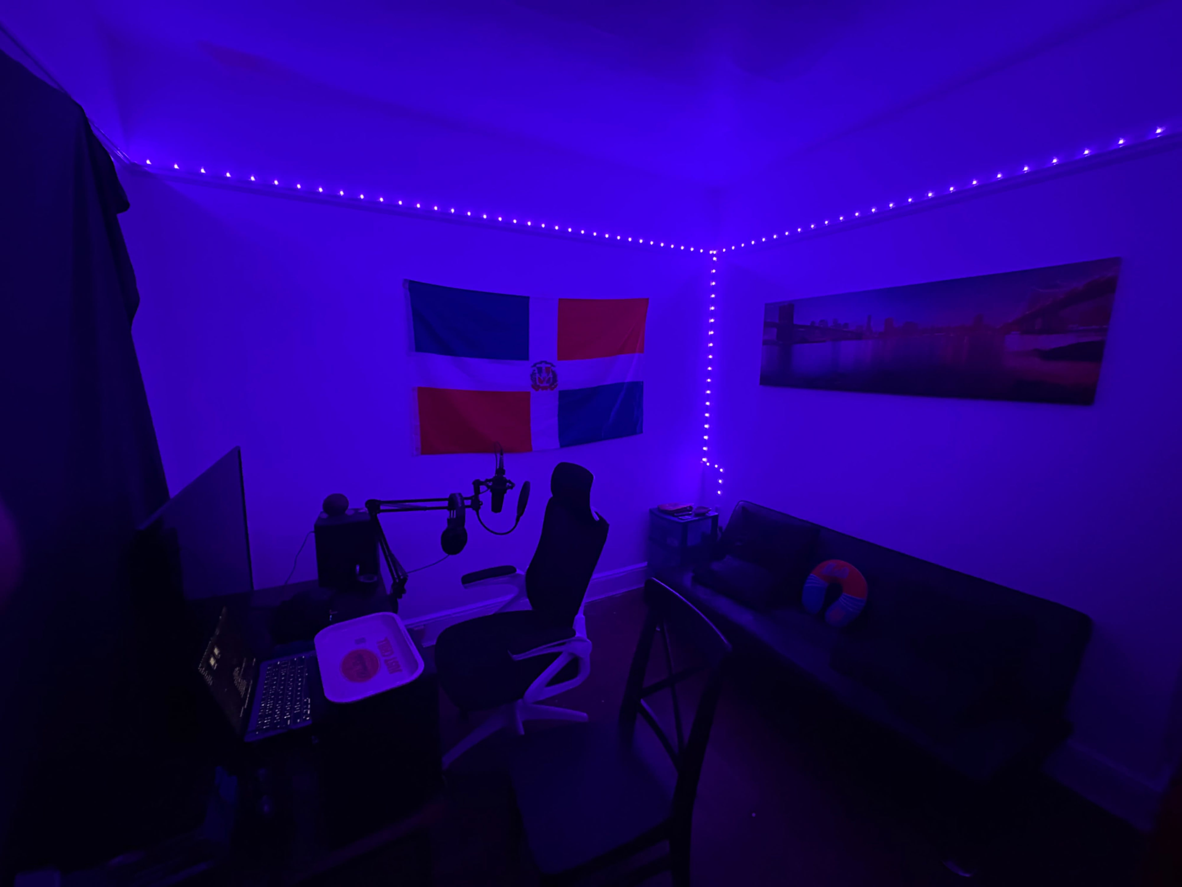The image shows a dimly lit room with purple LED lights, featuring a Dominican Republic flag on the wall, a desk with a computer setup, and a black sofa.