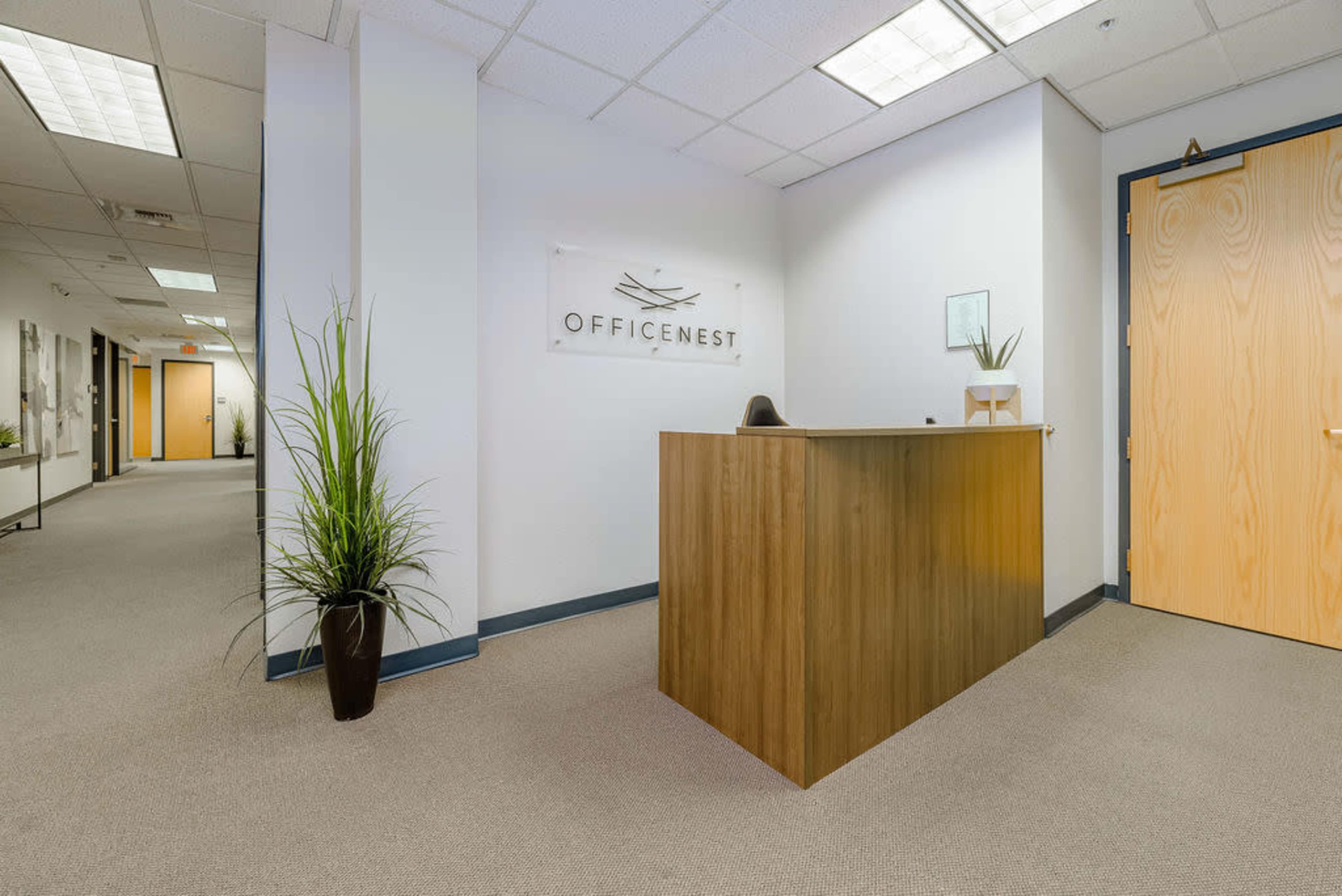 A reception area features a wooden front desk with a plant beside it and a wall-mounted sign that reads "OFFICENEST."