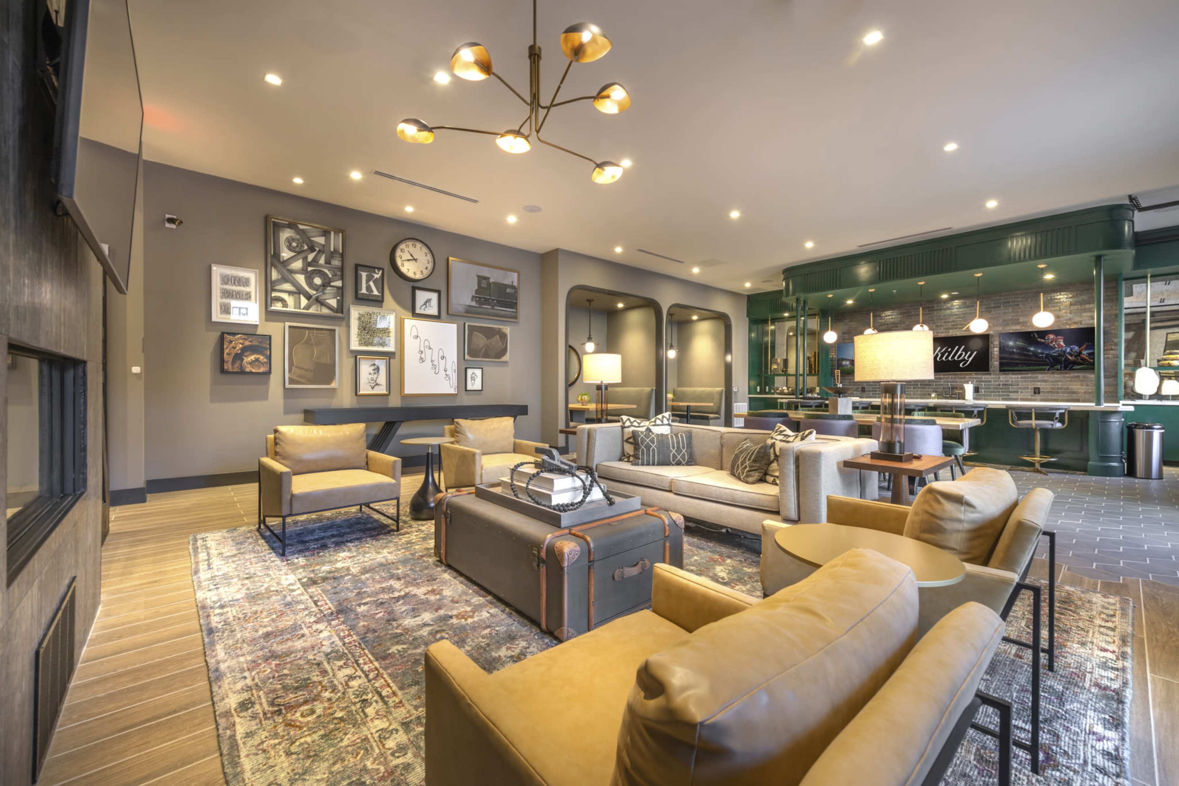 The image shows a modern lounge area with a mix of seating, decorative wall art, and a bar highlighted by soft lighting.