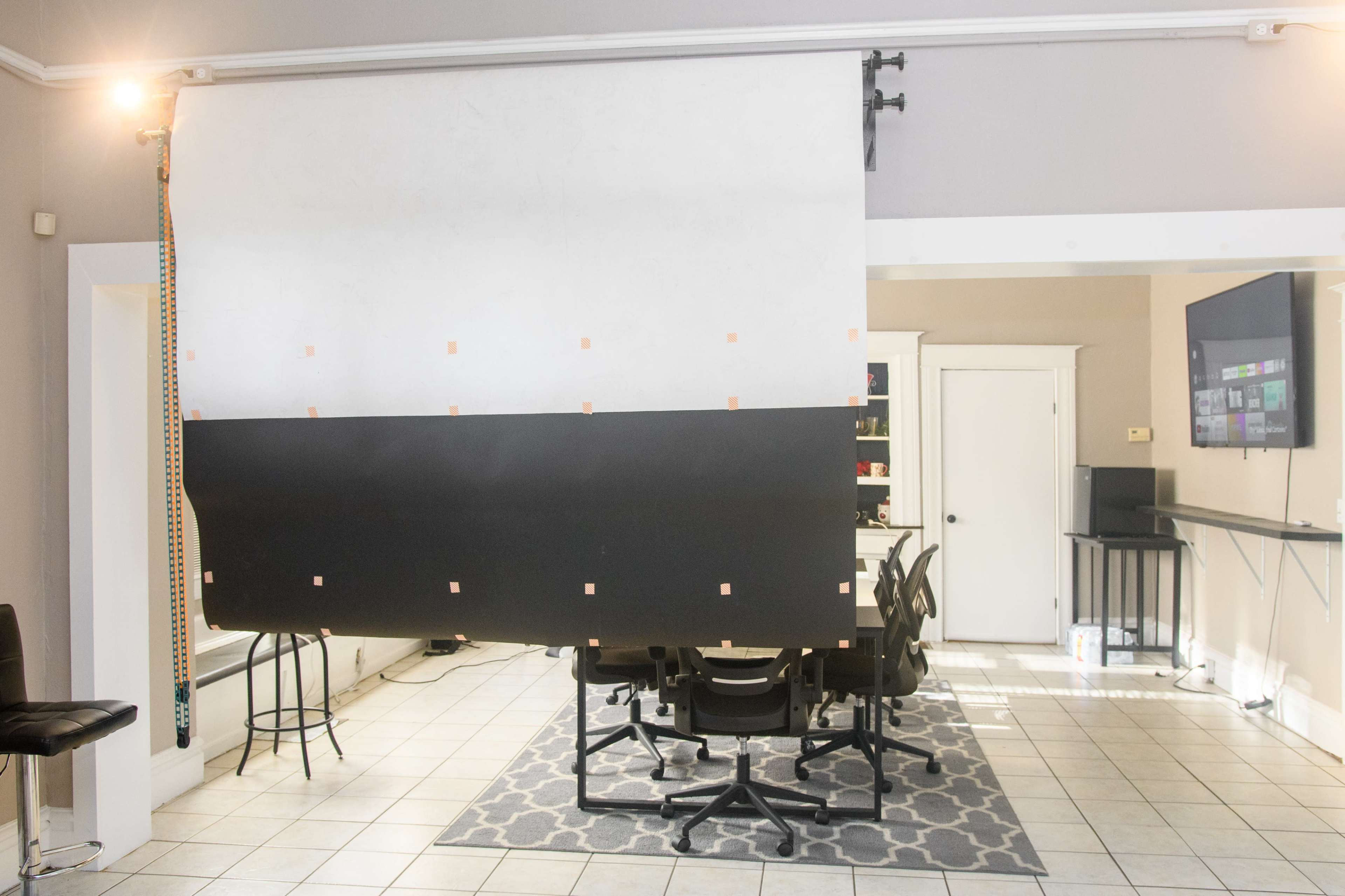 A large black and white backdrop is set up in a room with tiled flooring and several chairs arranged around a table.