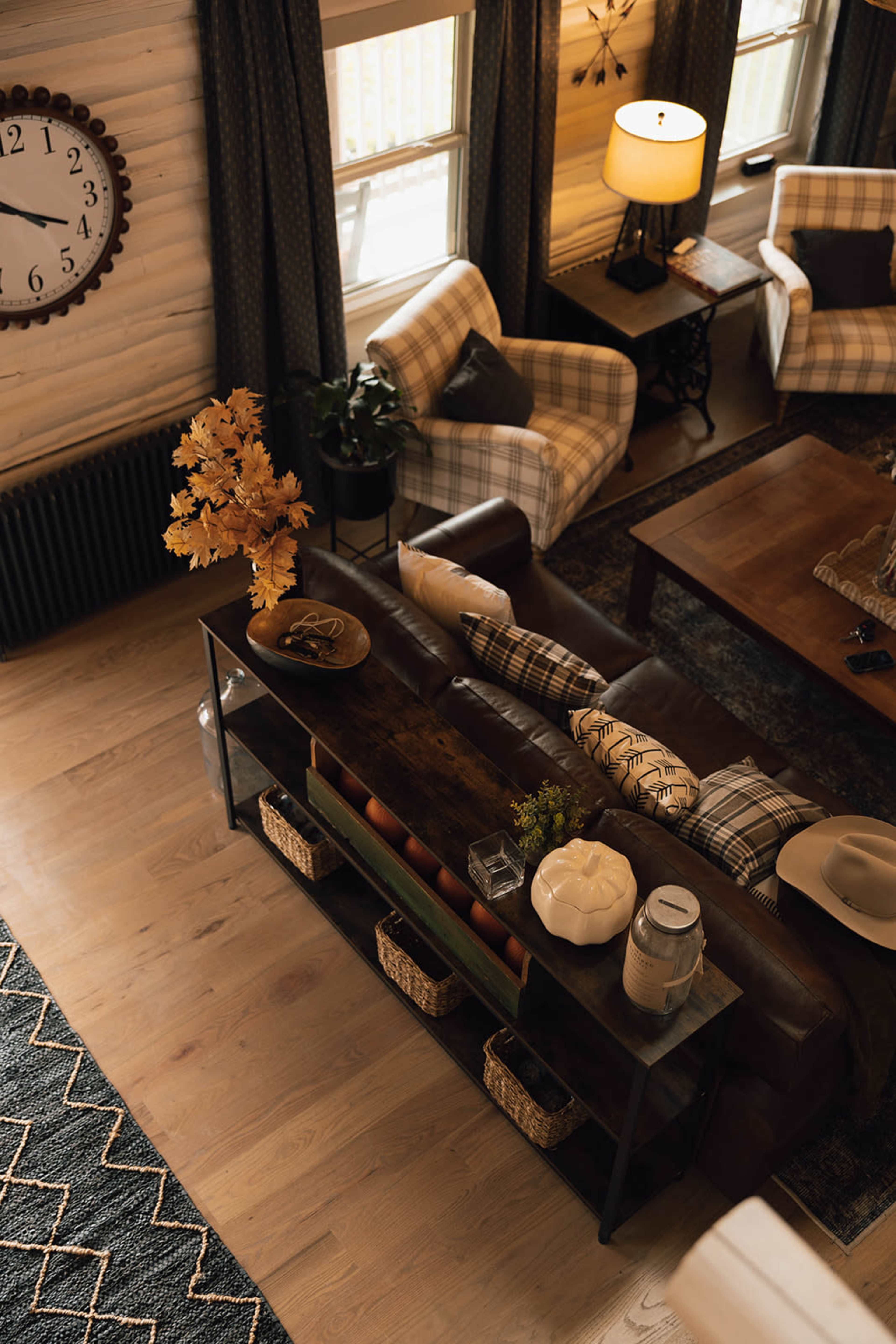A cozy living room features a leather sofa, a wooden coffee table, and a console table with decorative items, all complemented by patterned armchairs and warm lighting.