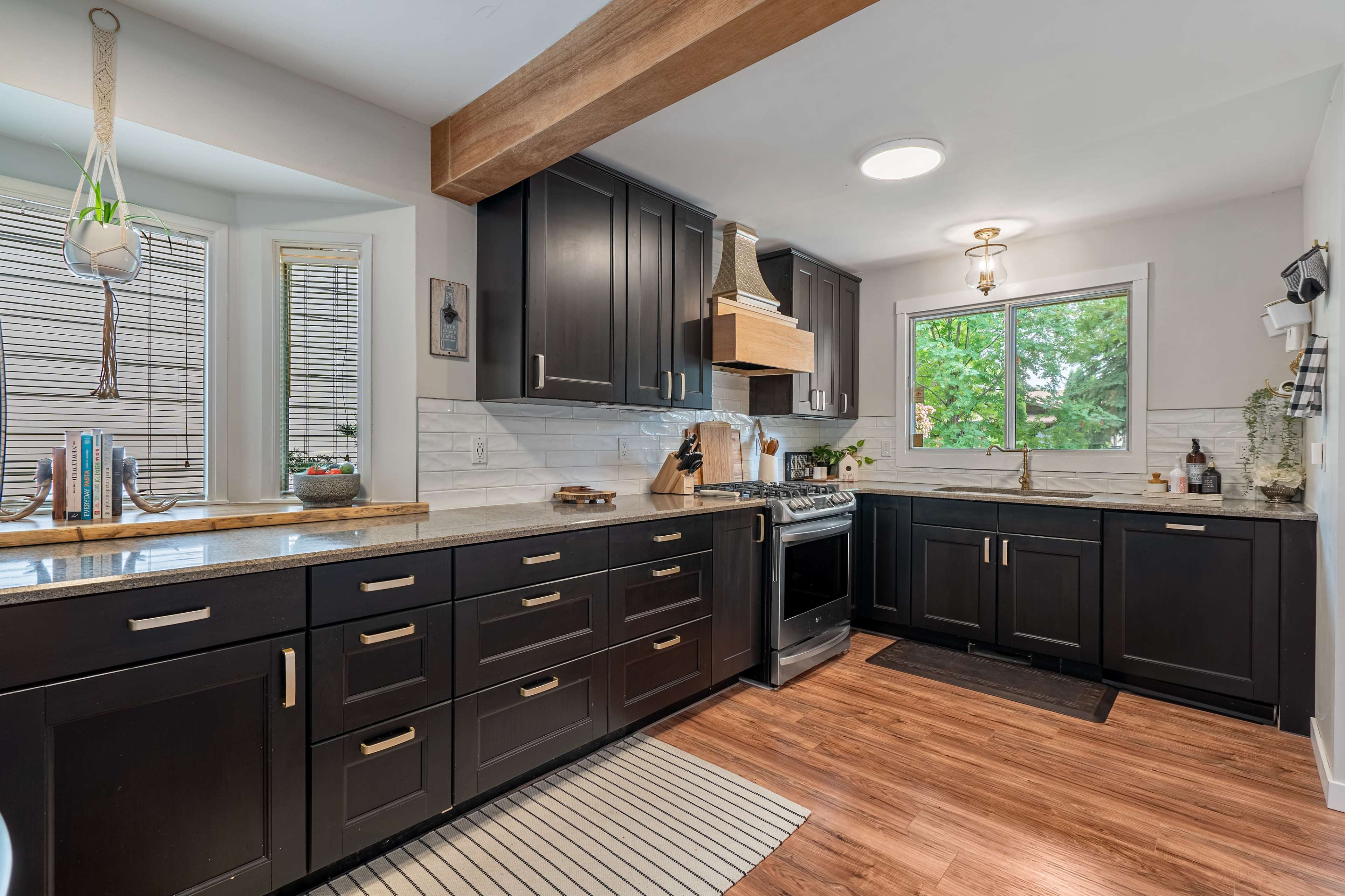 The kitchen features dark cabinetry, a central island, and large windows that offer natural light.