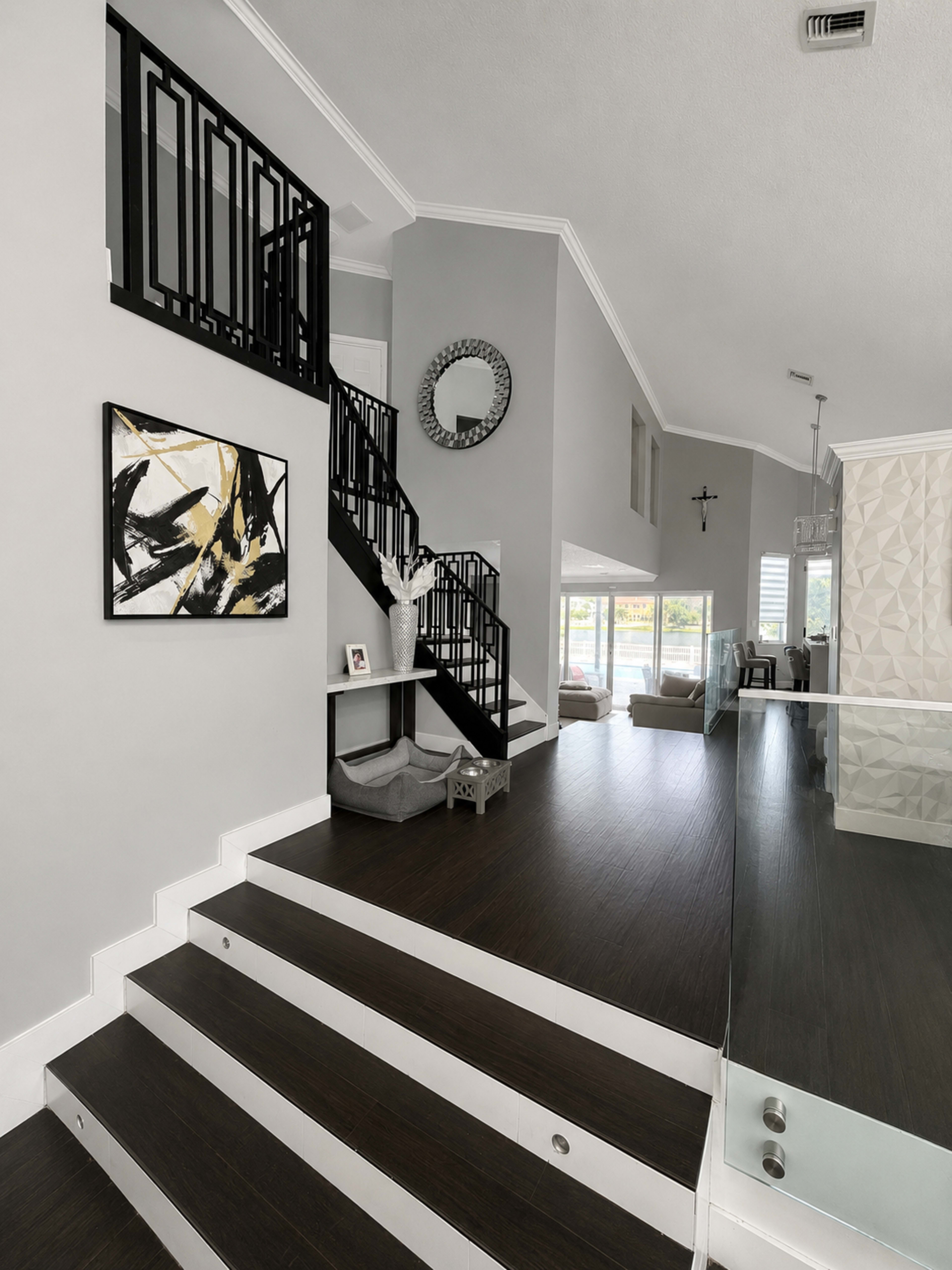 The image shows a modern entryway featuring a staircase with black railings, a round mirror, and decorative artwork on the wall.