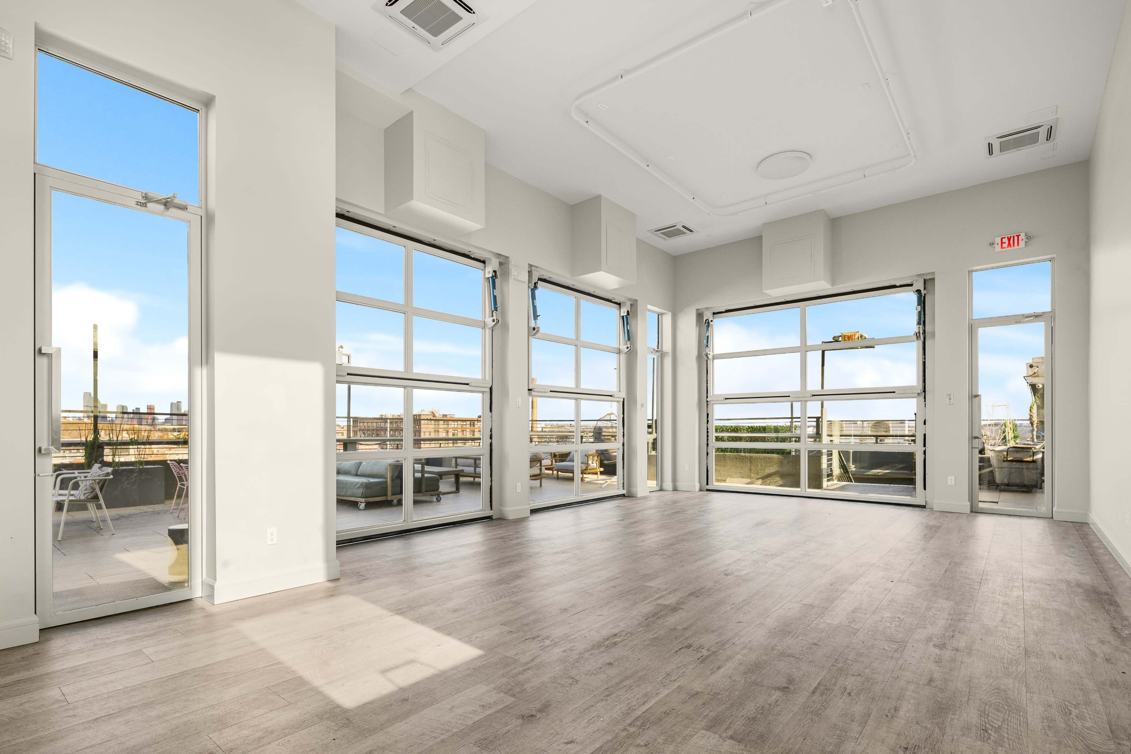 A spacious room with large windows providing ample natural light and views of an outdoor terrace.