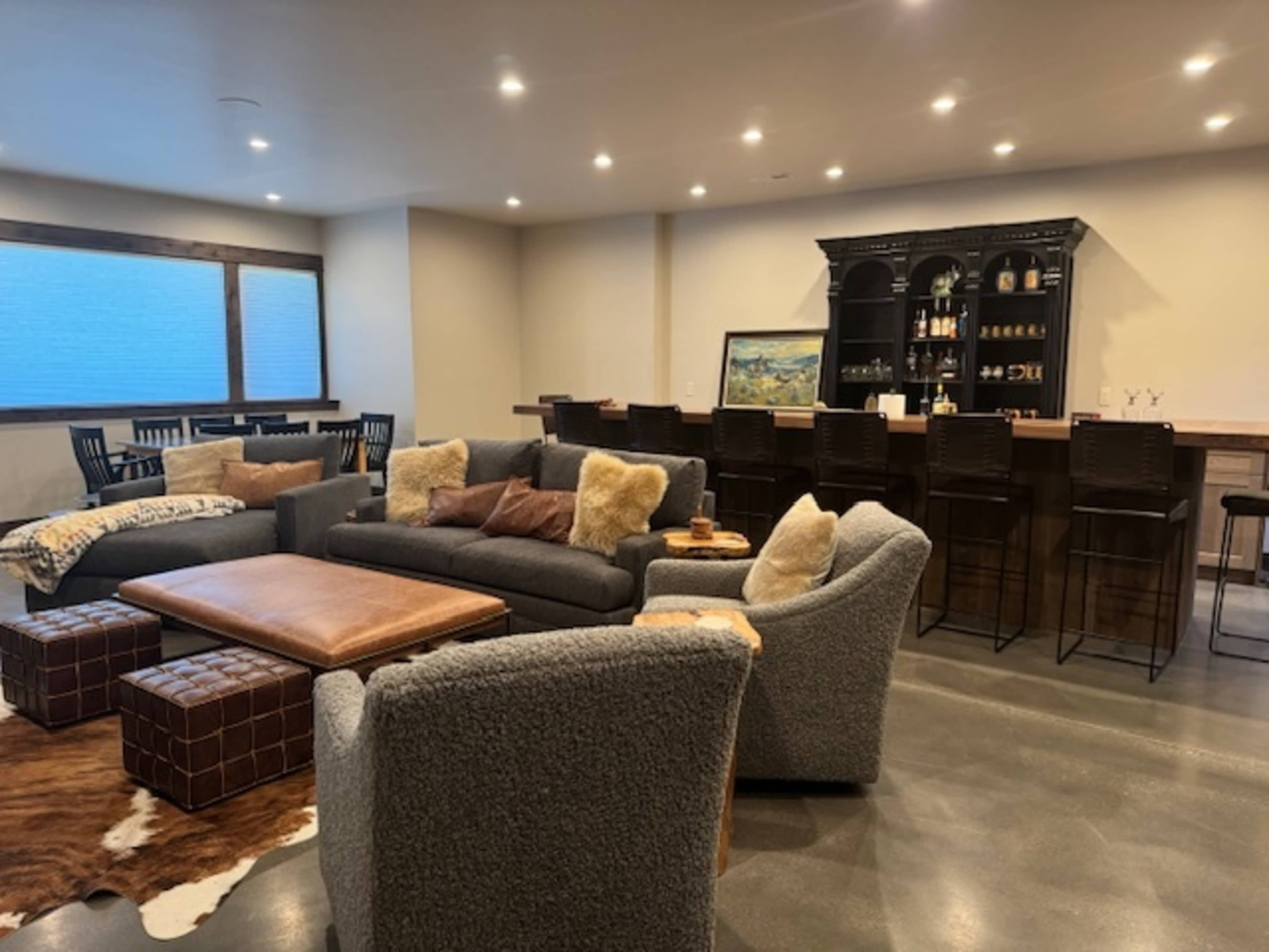 The image shows a modern, well-lit lounge area with a gray sectional sofa, a coffee table, and a bar with high stools against a wall.