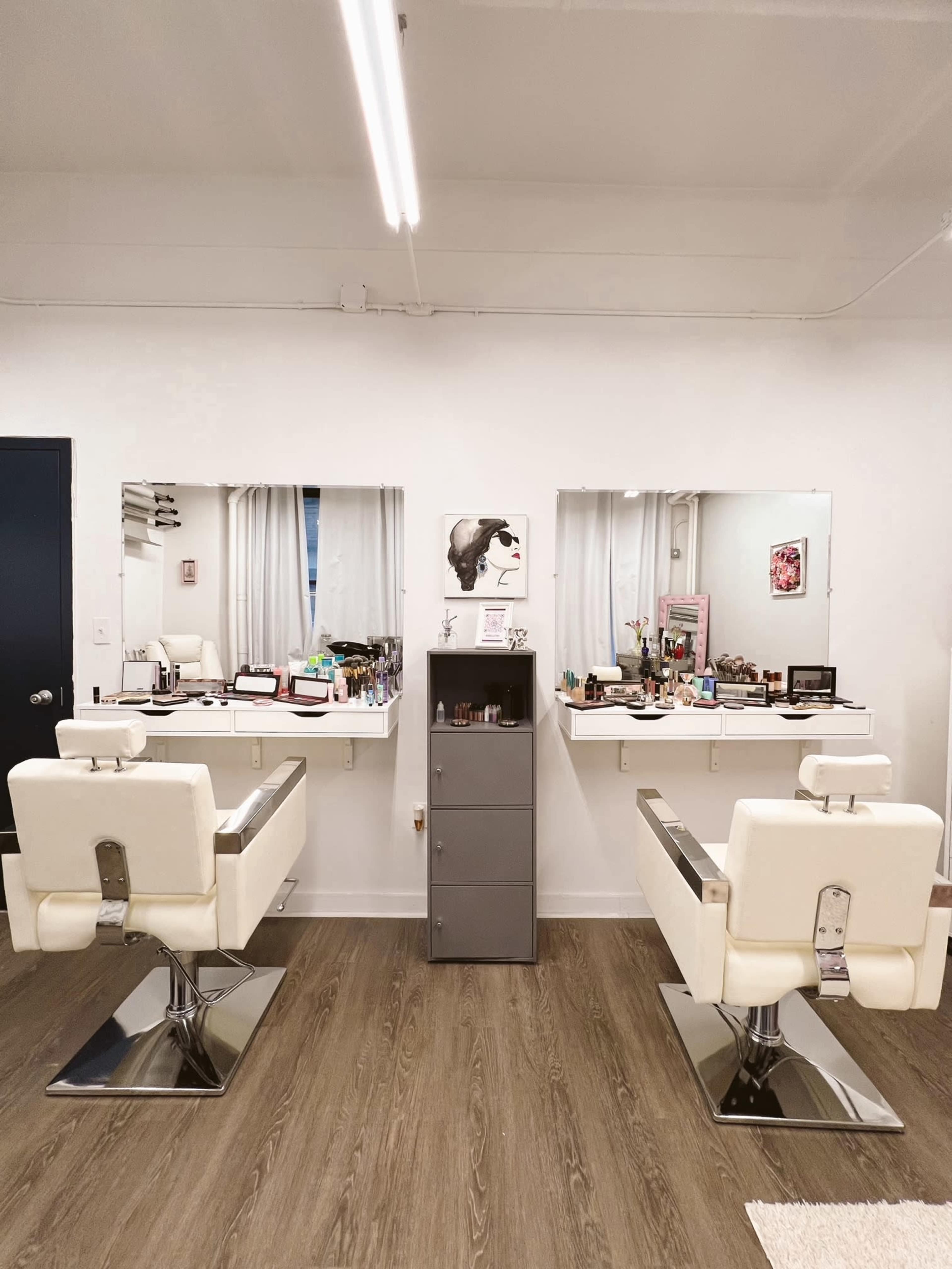 A modern hair salon with two white styling chairs, large mirrors above each station, and a gray storage cabinet in the center.
