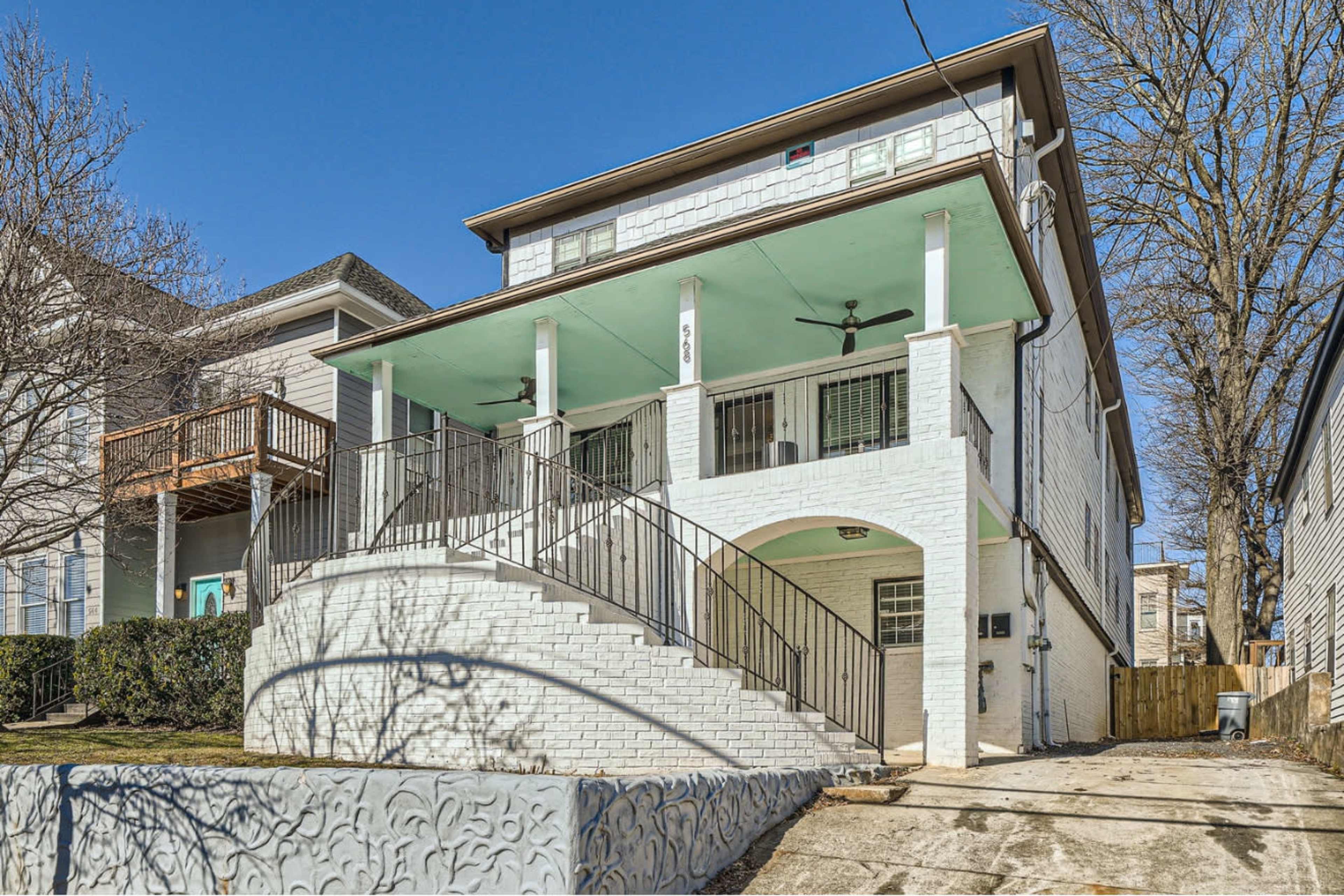 The image shows a three-story white house with a covered porch, a curved staircase, and a landscaped front yard.