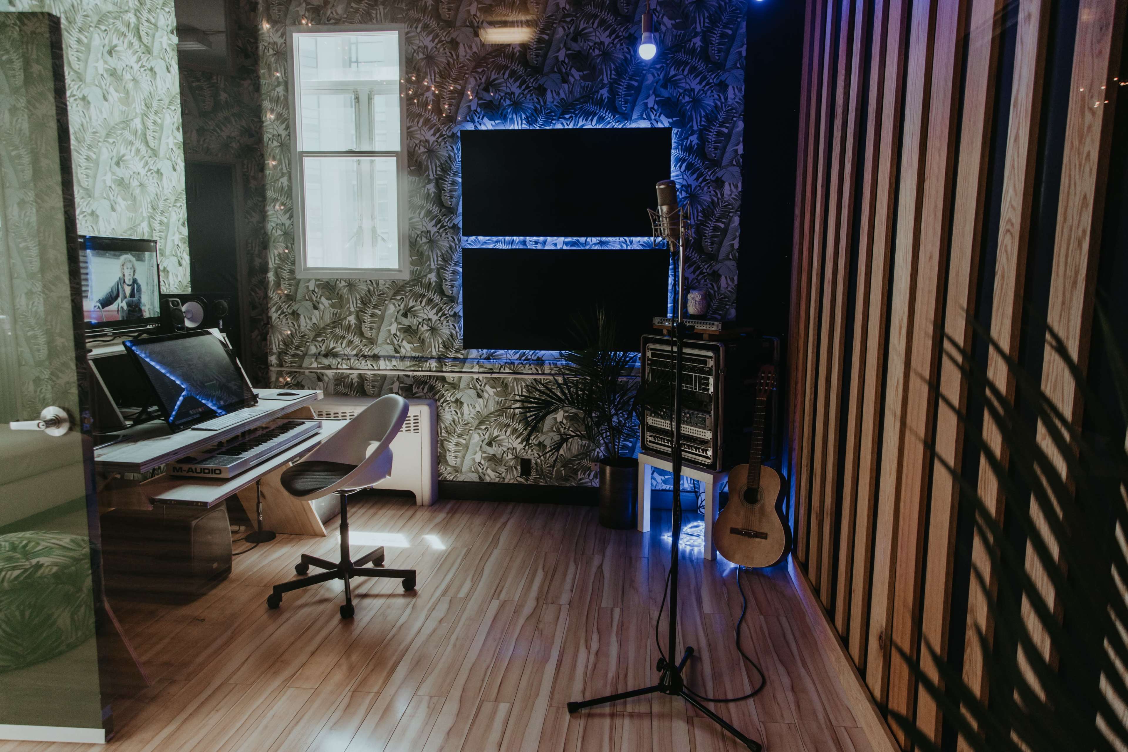 A modern home studio with a desk, computer, microphone, and acoustic panels on the walls.