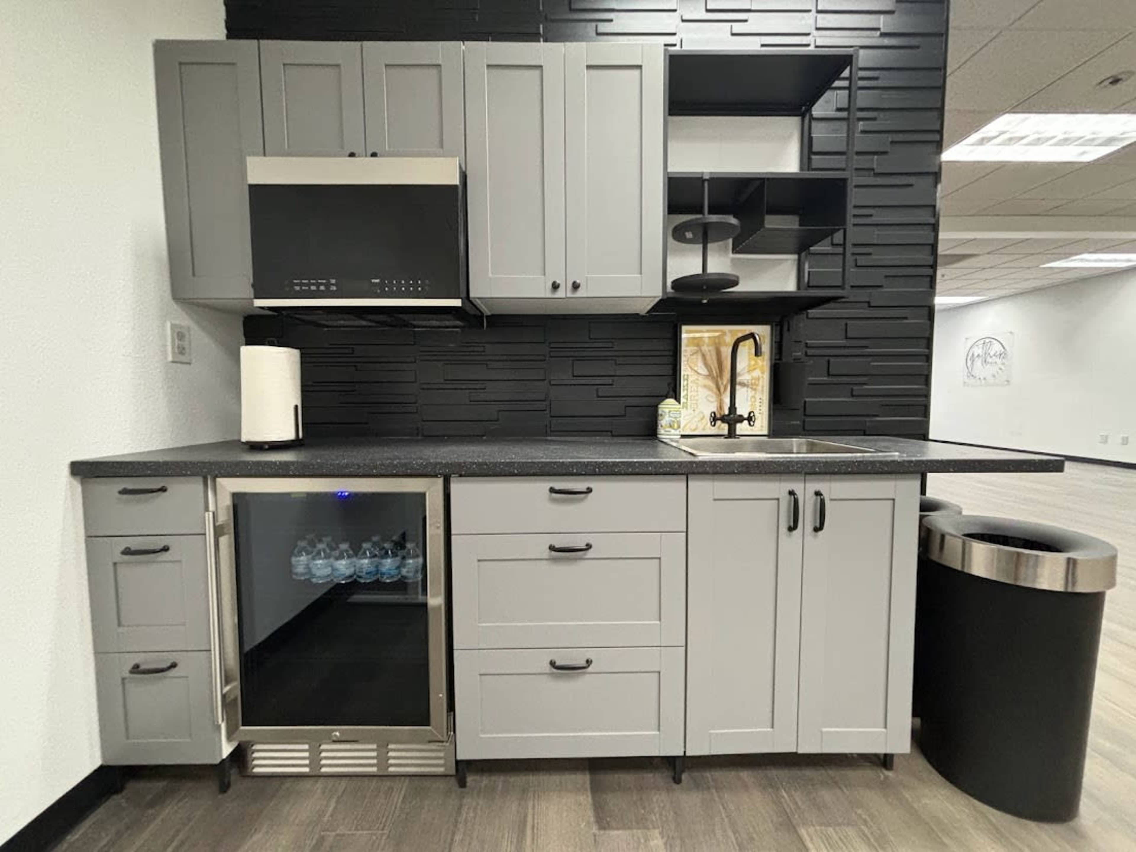 A modern kitchen arrangement featuring gray cabinets, a stainless steel refrigerator, a sink, and a black shelving unit against a textured wall.