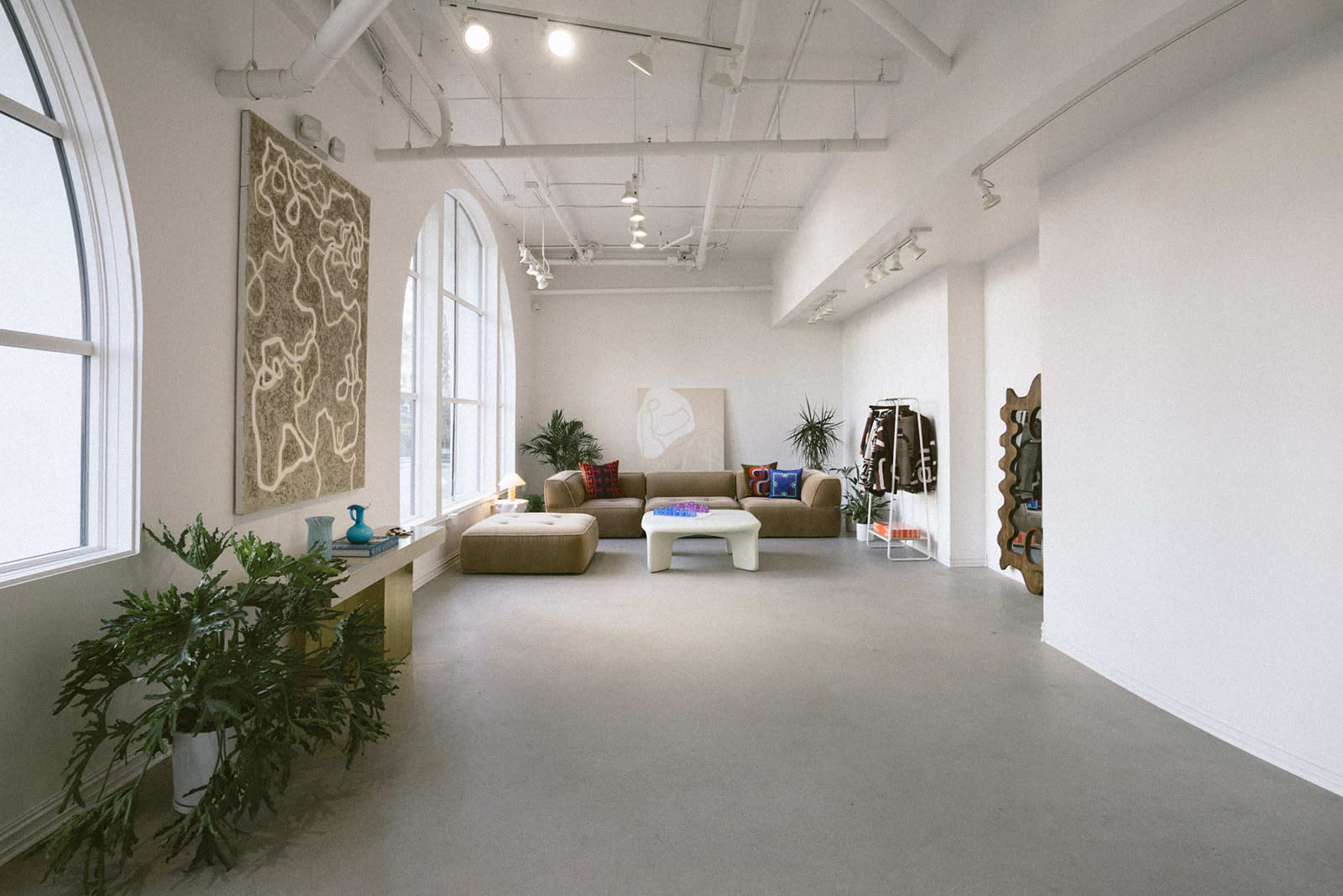 A spacious, minimalist gallery-like room features a large window, a brown sofa, a coffee table, and modern art on the walls.