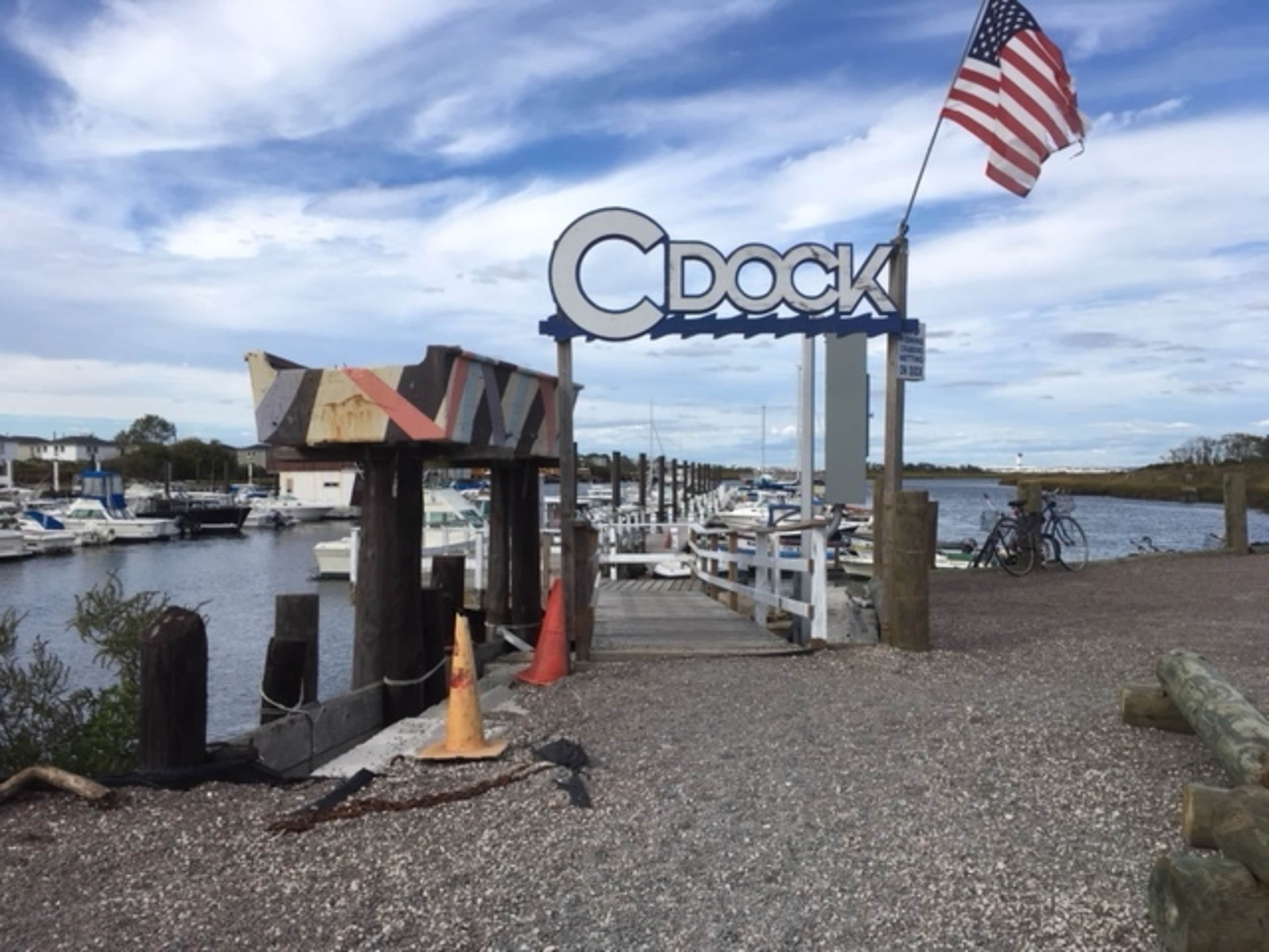 The image shows a dock area with boats moored along the water, a sign that reads "C DOCK," and an American flag flying overhead.