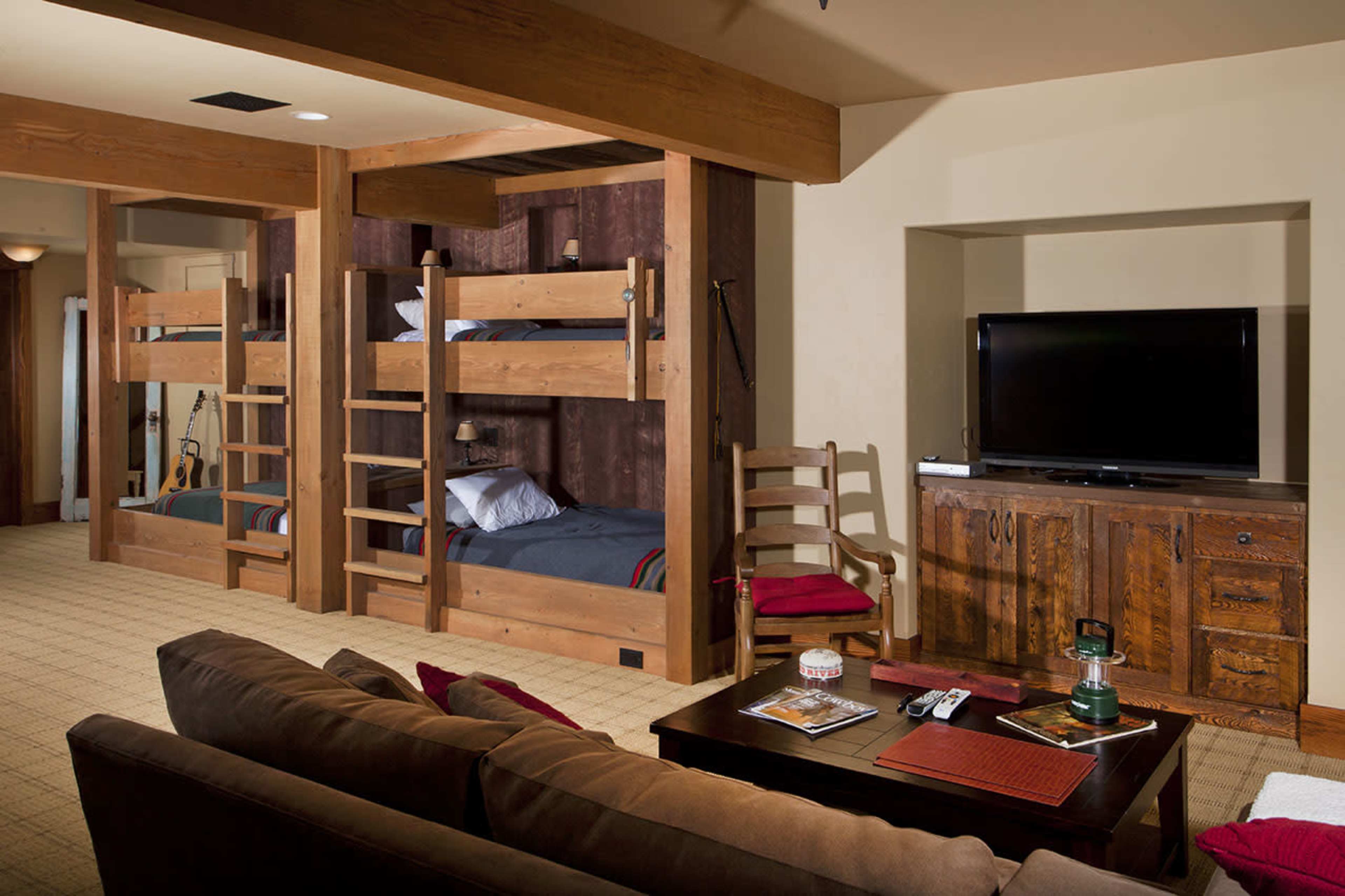 A cozy room featuring two sets of wooden bunk beds, a television, and a comfortable seating area with a coffee table.