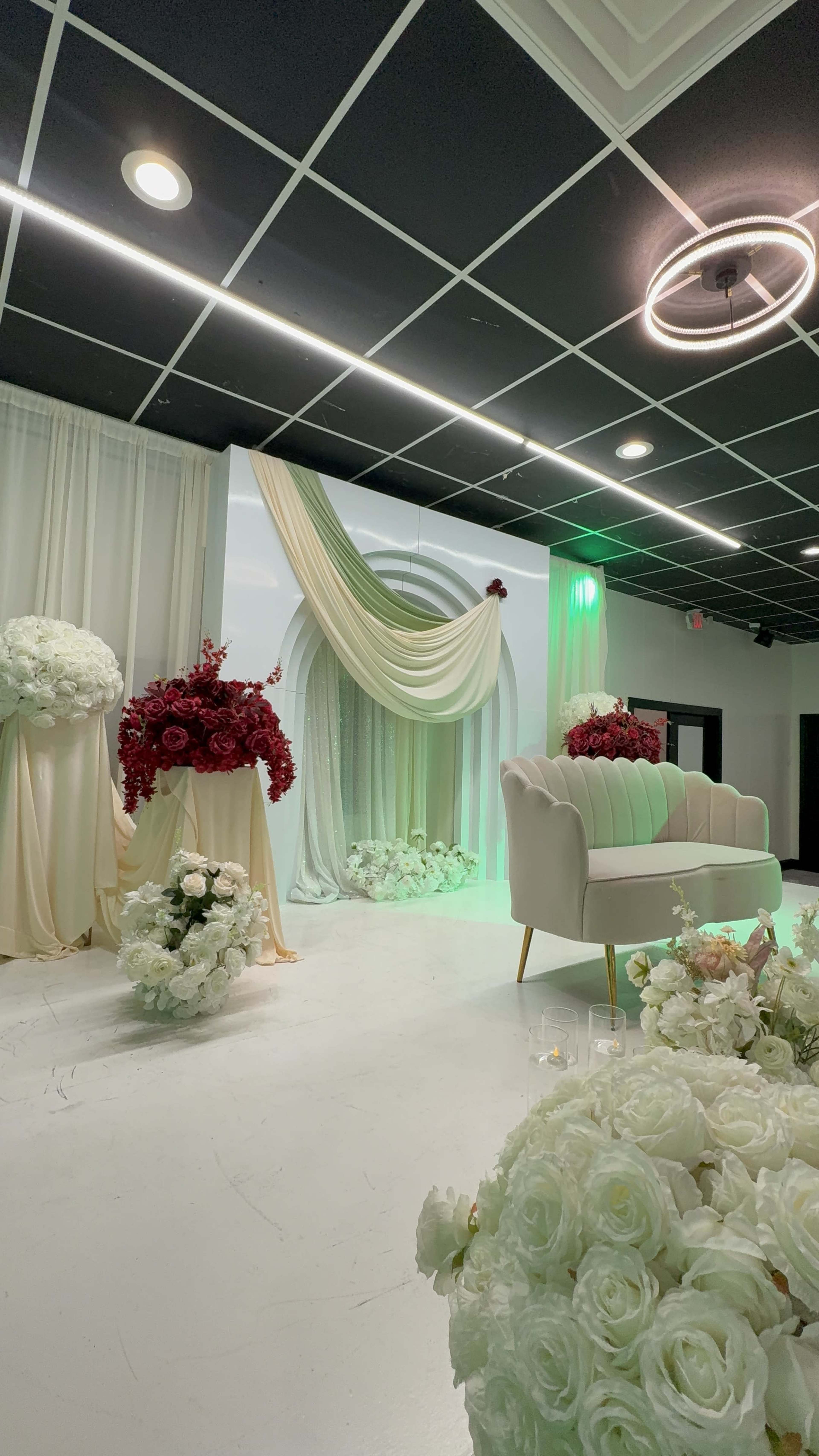 The scene features an elegantly decorated interior with a light-colored couch, floral arrangements of red and white blooms, and draped fabric creating a backdrop suitable for an event.