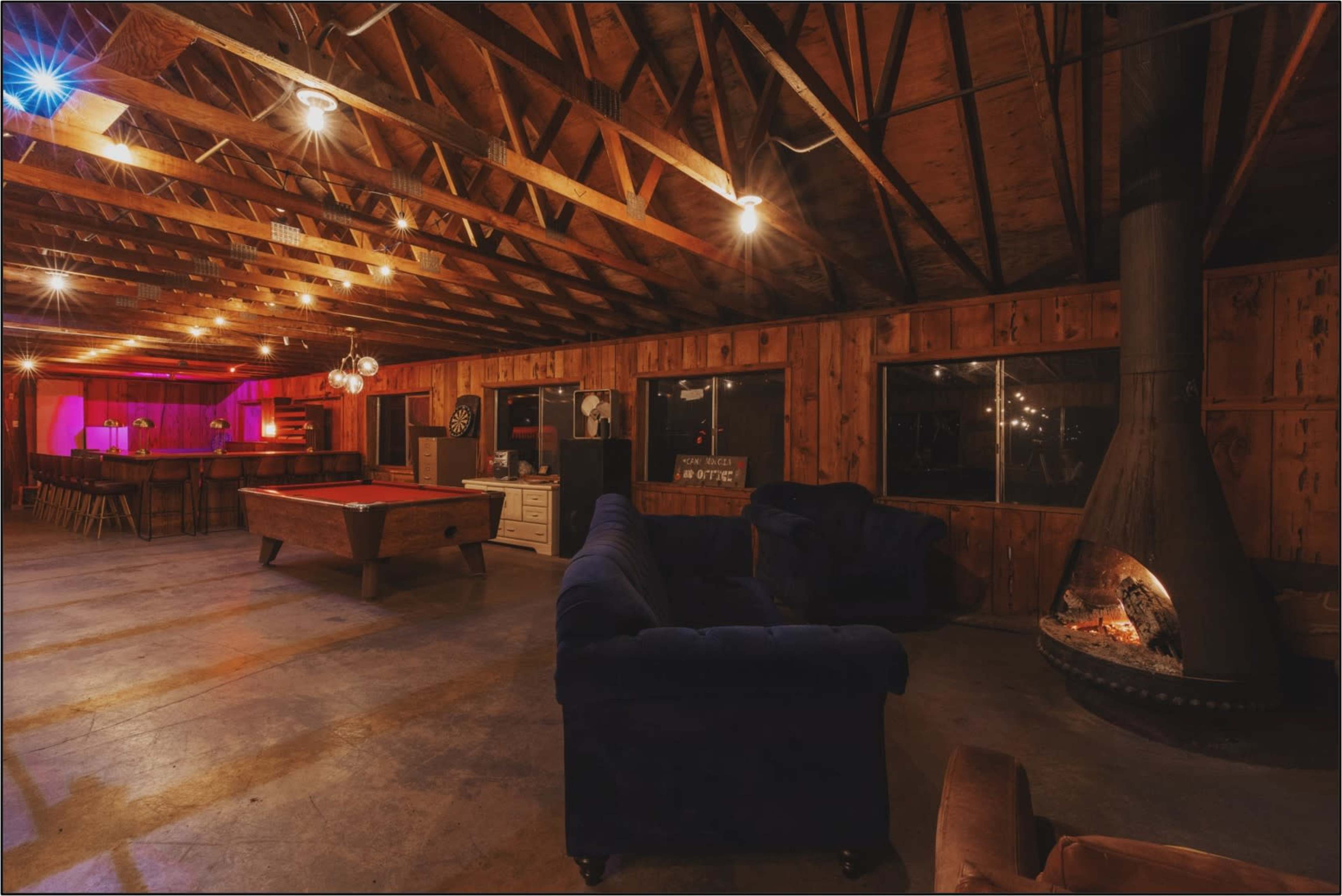 A spacious interior of a rustic room with wooden walls, exposed beams, a pool table, and a fireplace.