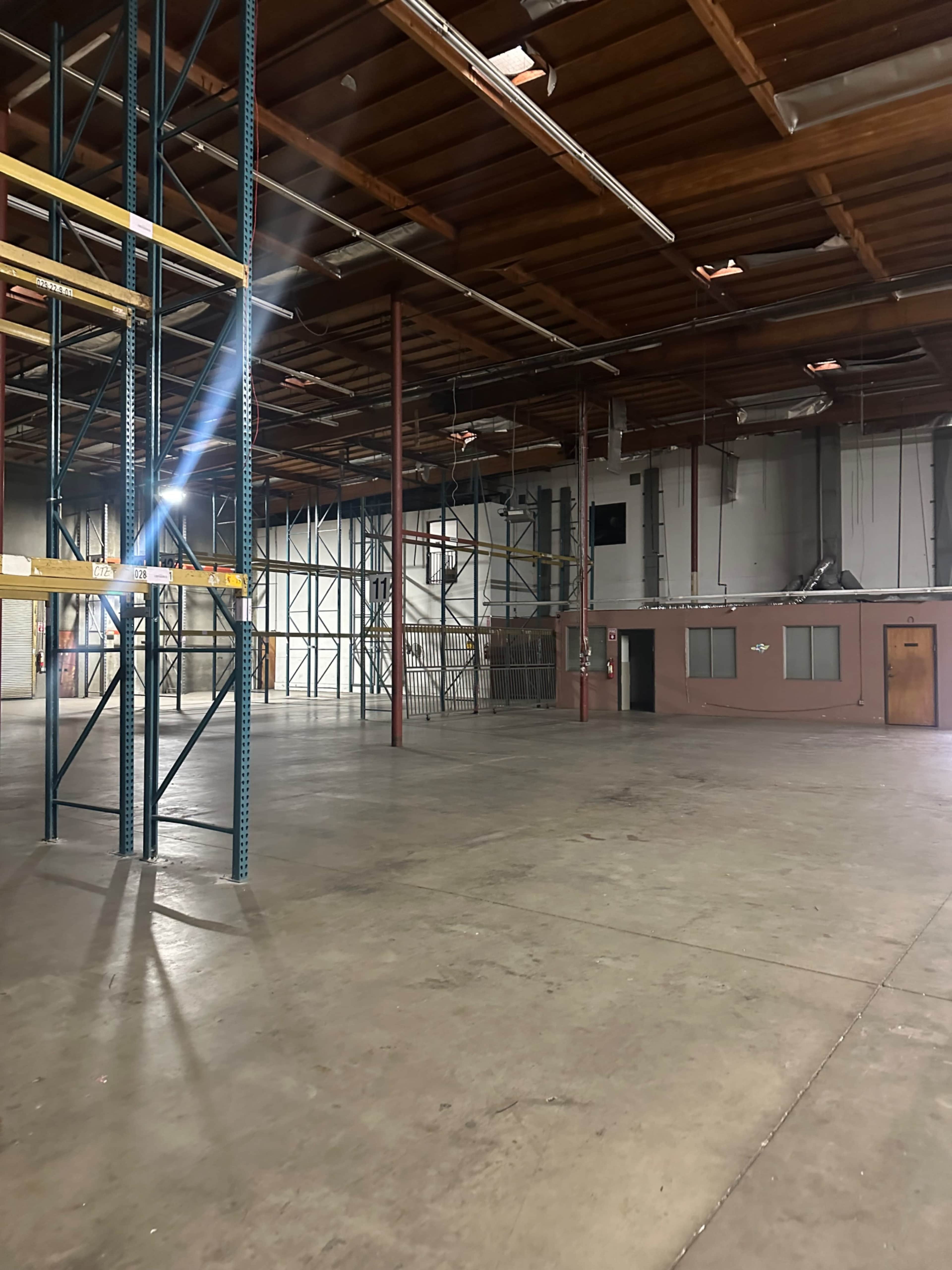 The image shows a large, empty warehouse space with metal shelving units and a concrete floor.