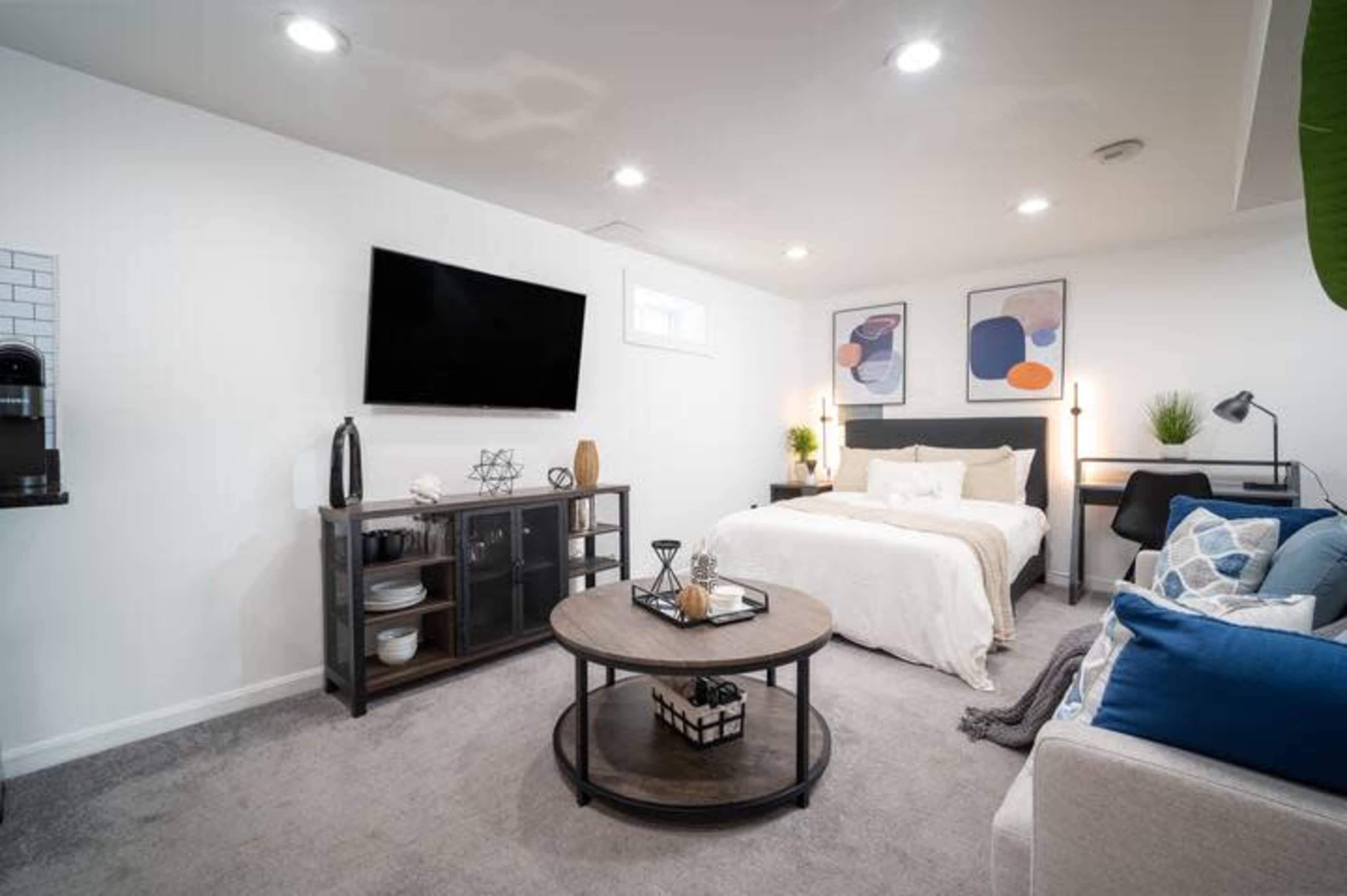A modern studio apartment features a bed against a wall, a television mounted above, and a seating area with a coffee table and decorative elements.
