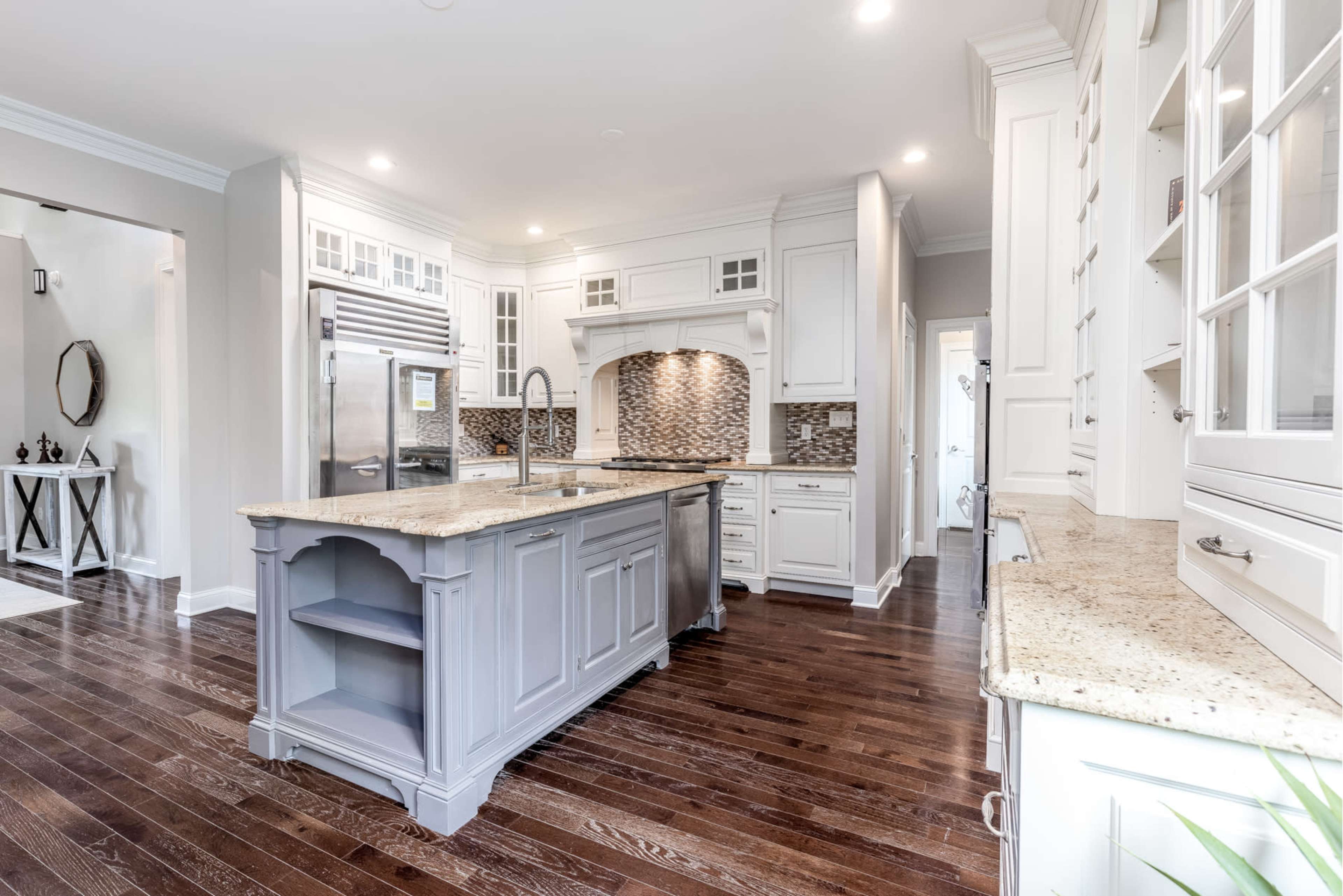 A modern kitchen with white cabinetry, a large central island, and dark hardwood floors.