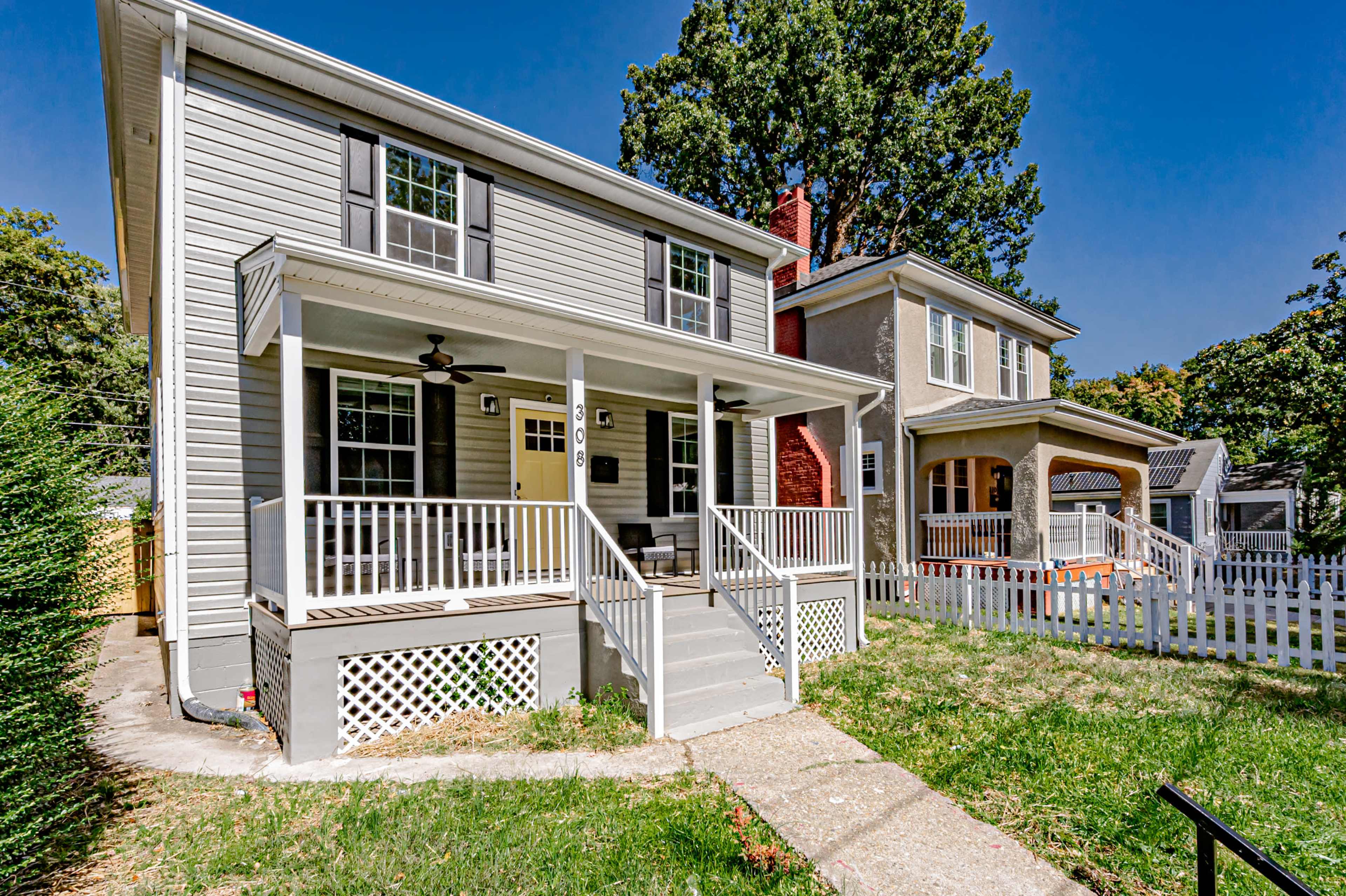 Two neighboring two-story houses with porches, surrounded by green grass and trees under a clear blue sky.