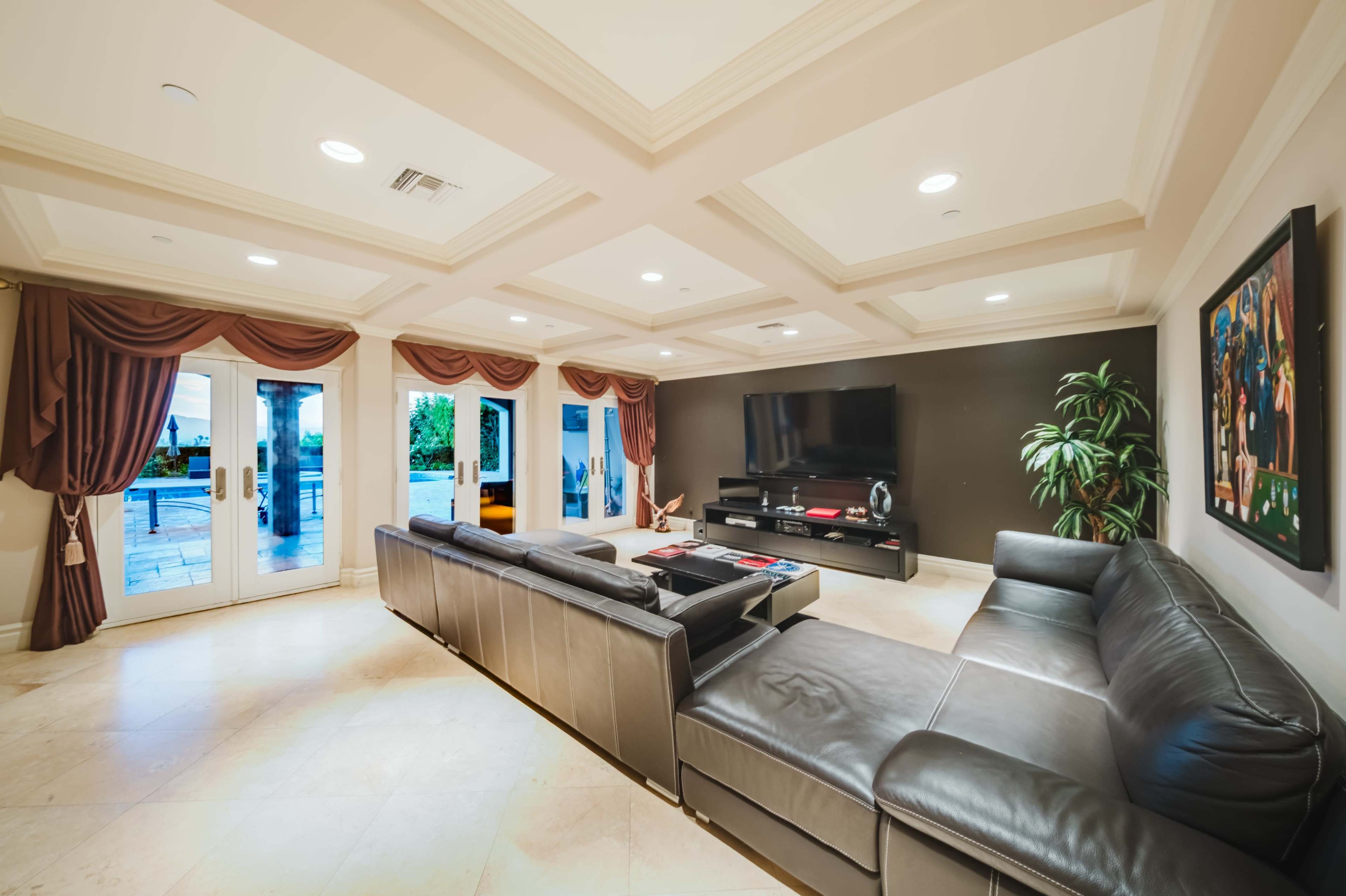 The image shows a spacious living room with a large sectional sofa, a wall-mounted television, and sliding glass doors leading to an outdoor area.