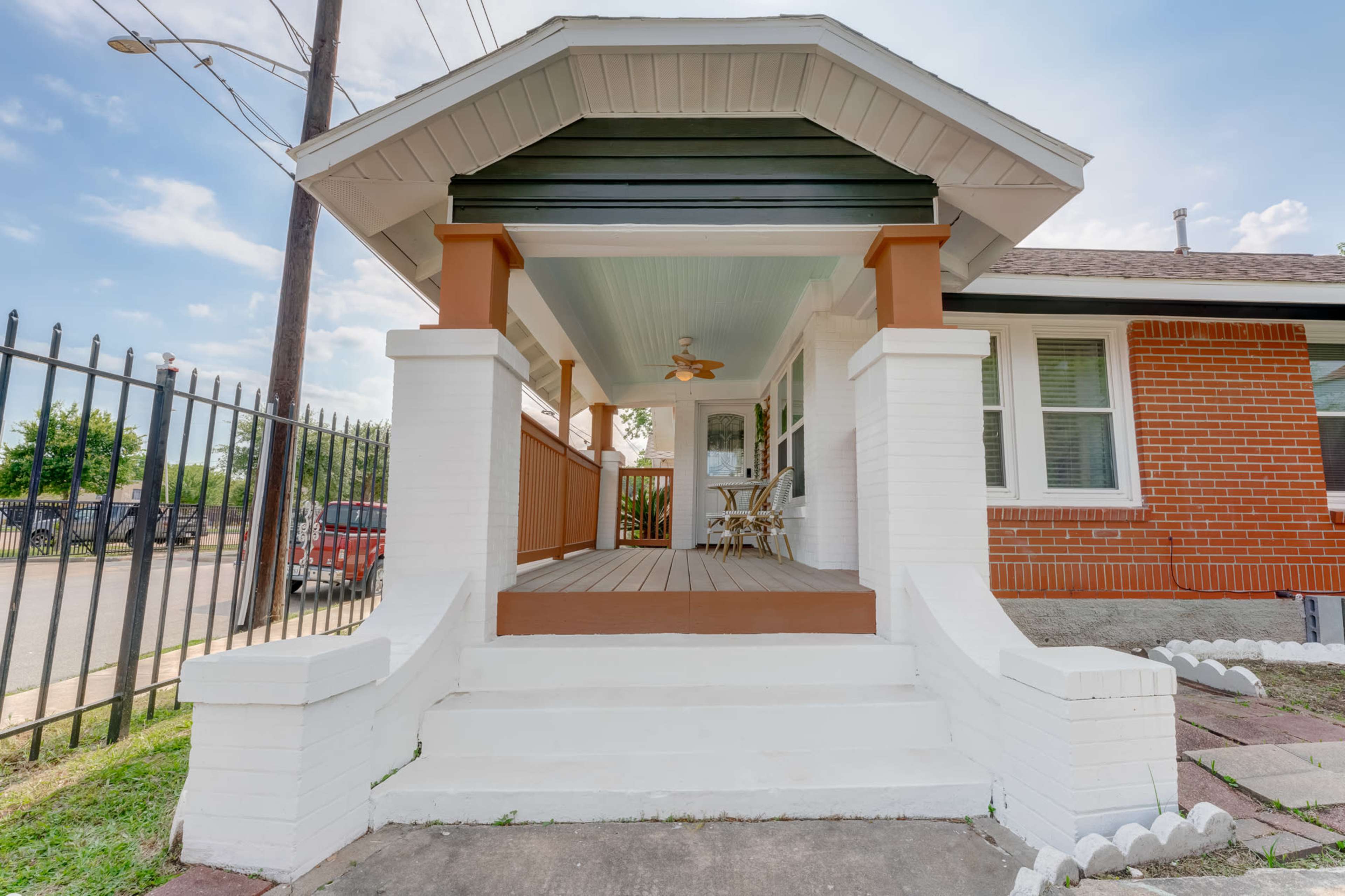 A porch with a wooden floor, white brick columns, and a ceiling fan, leading to a brick house.