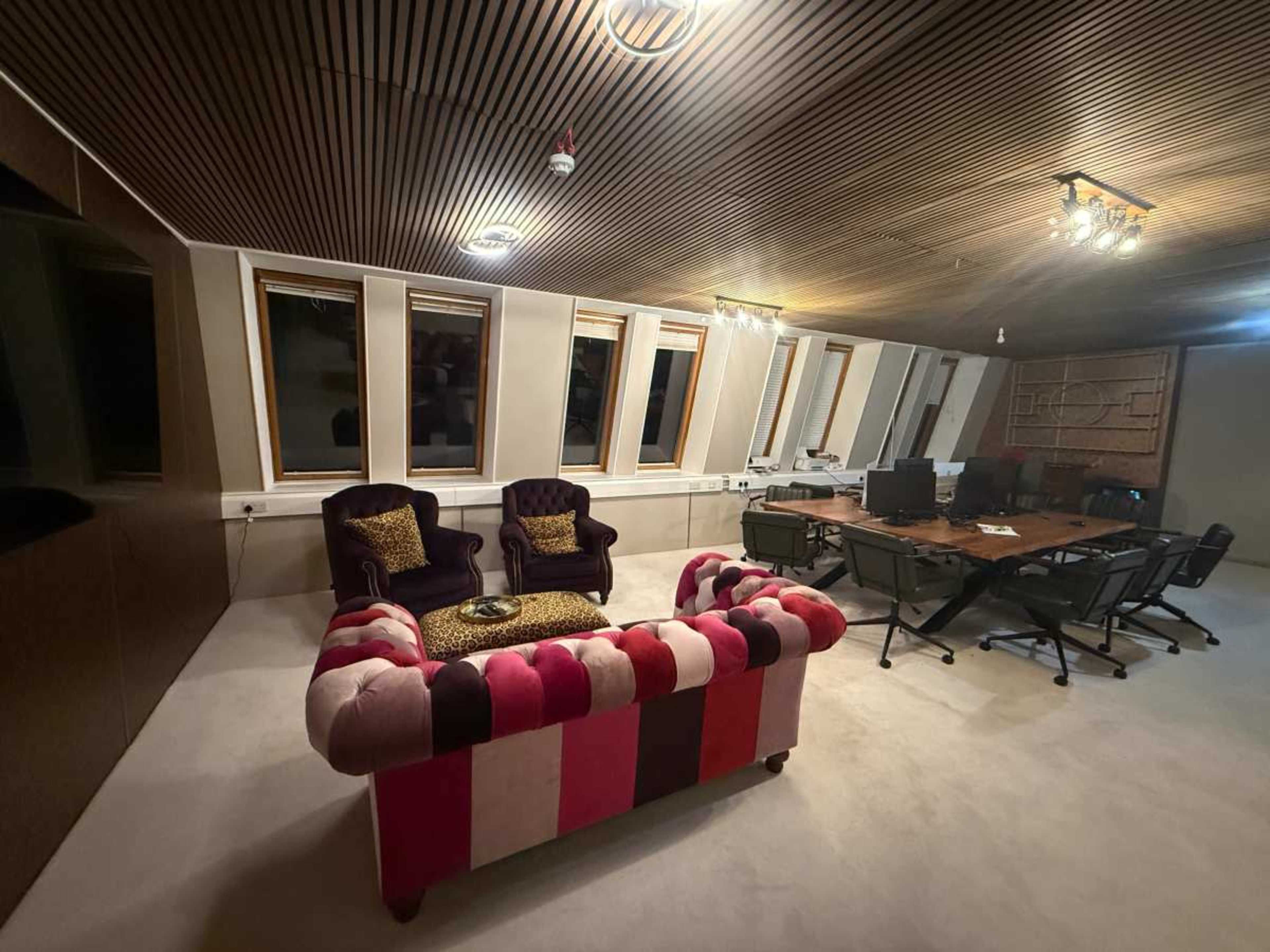 The image shows a modern office space featuring a pink and patterned sofa, two purple chairs, and a large conference table surrounded by black office chairs.