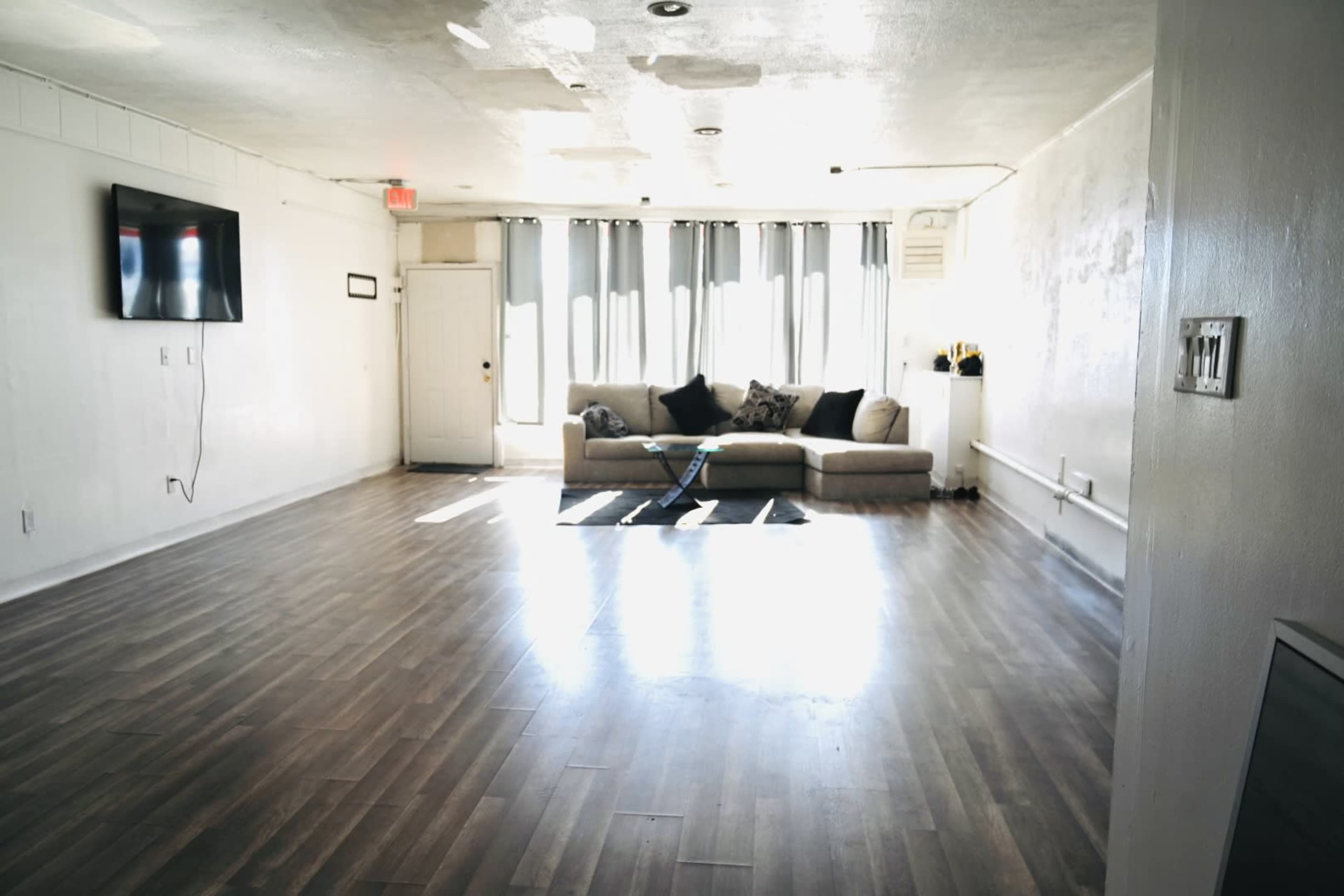 A spacious, empty room with a gray couch against the wall and a television mounted on the opposite wall.