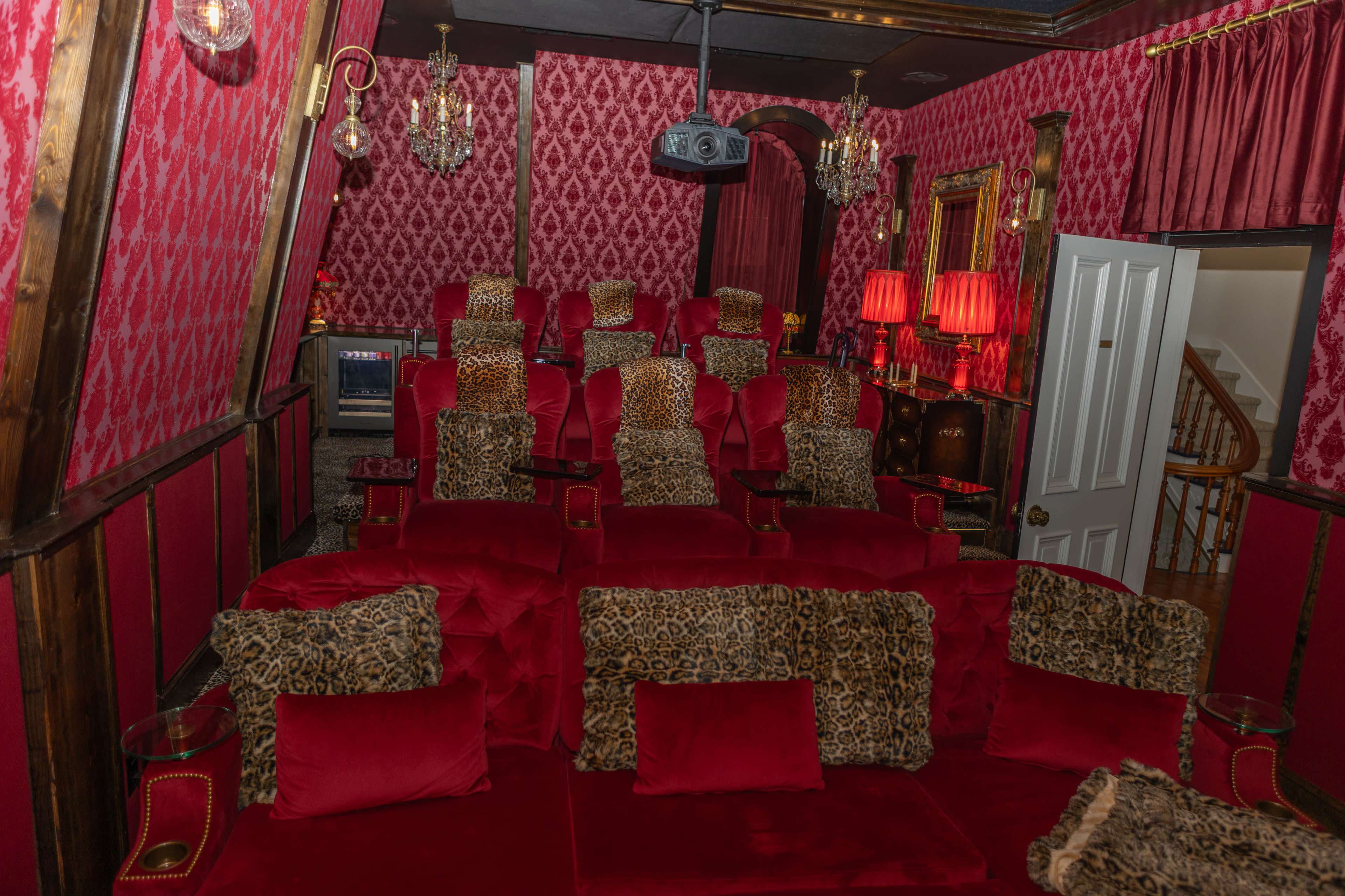 The image shows a small, richly decorated home theater with plush red seating, leopard-print accents, and ornate lighting fixtures.