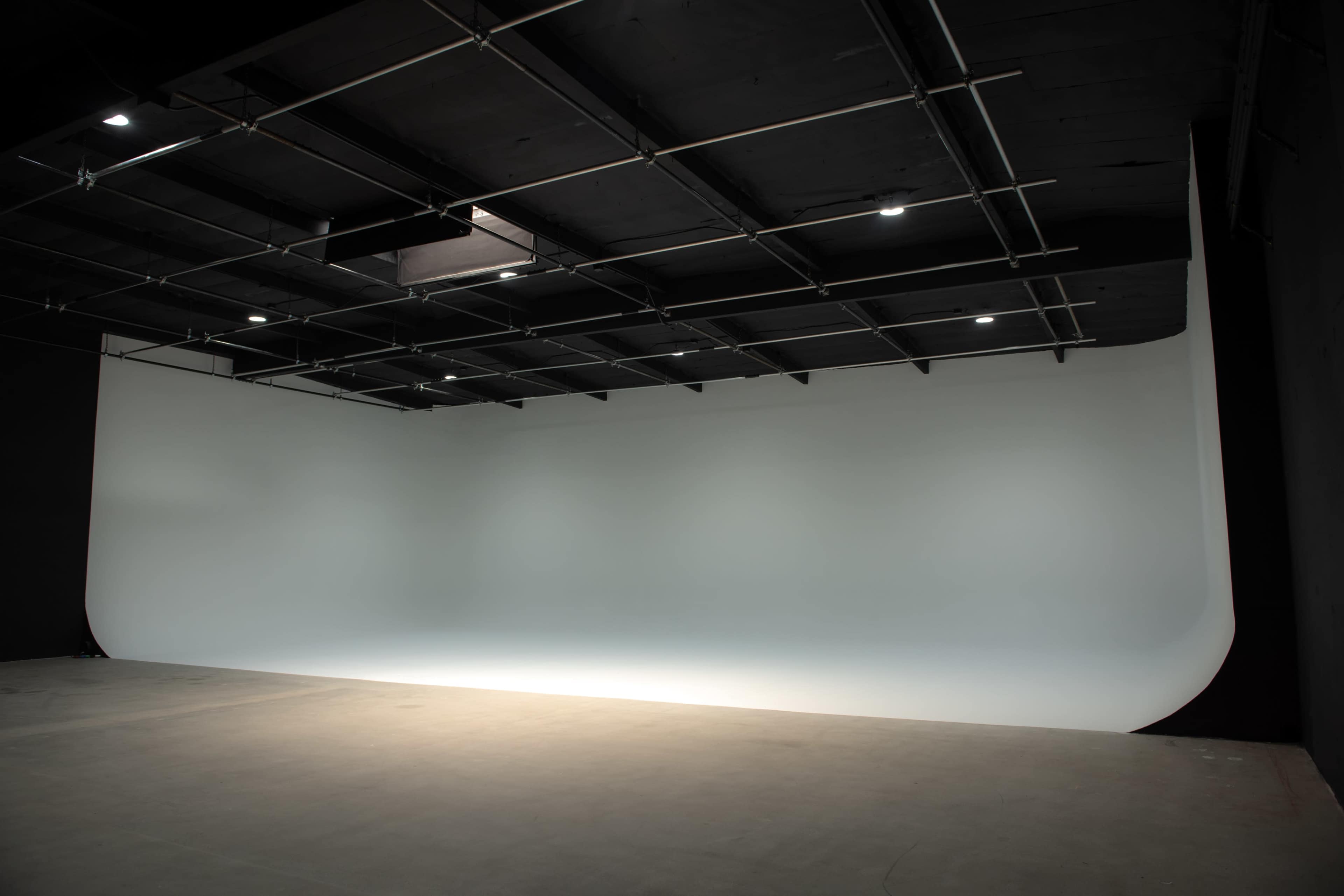 A spacious studio with a seamless white backdrop and a dark ceiling.