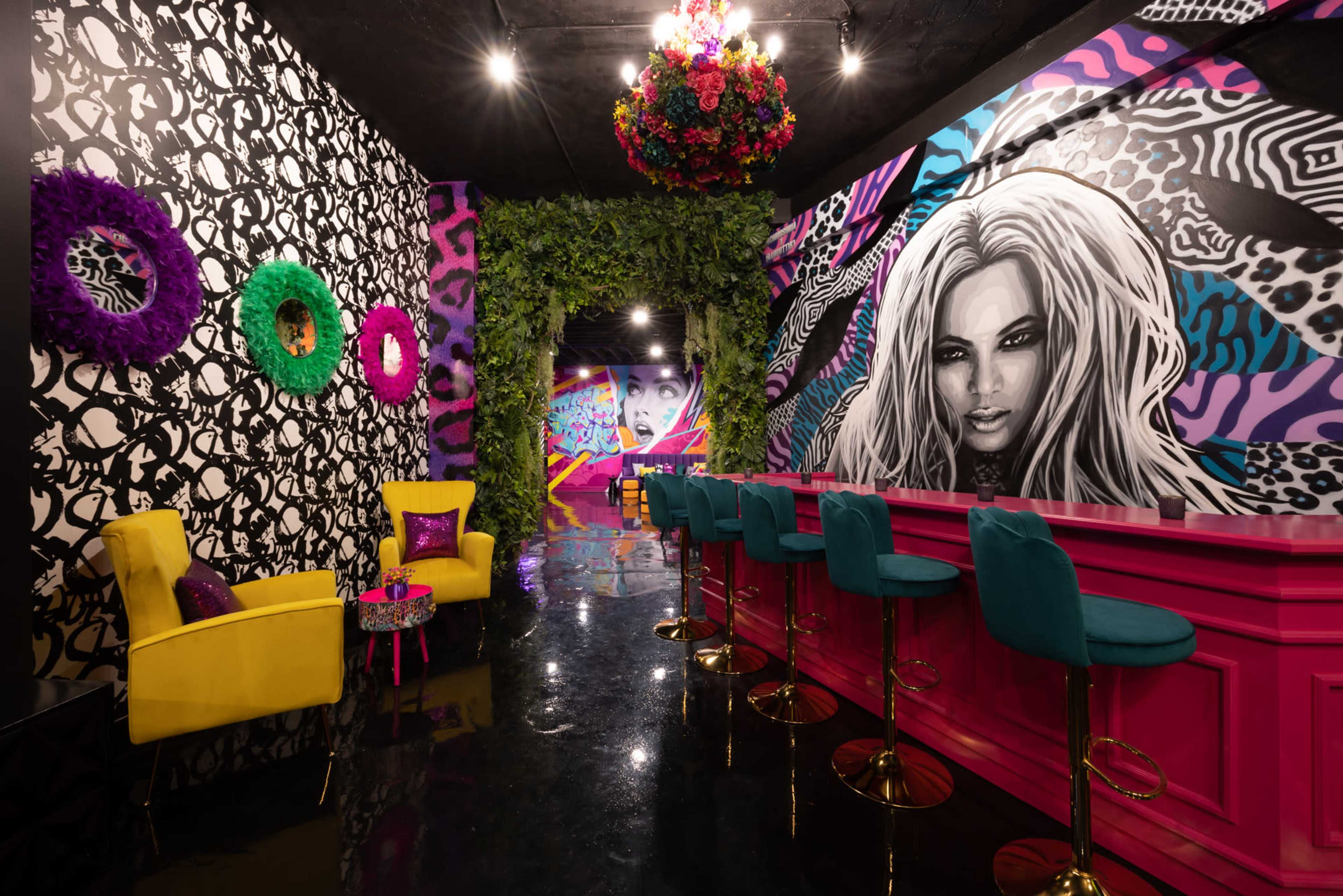 A colorful interior space with vibrant murals, patterned walls, and a pink bar with teal seating.