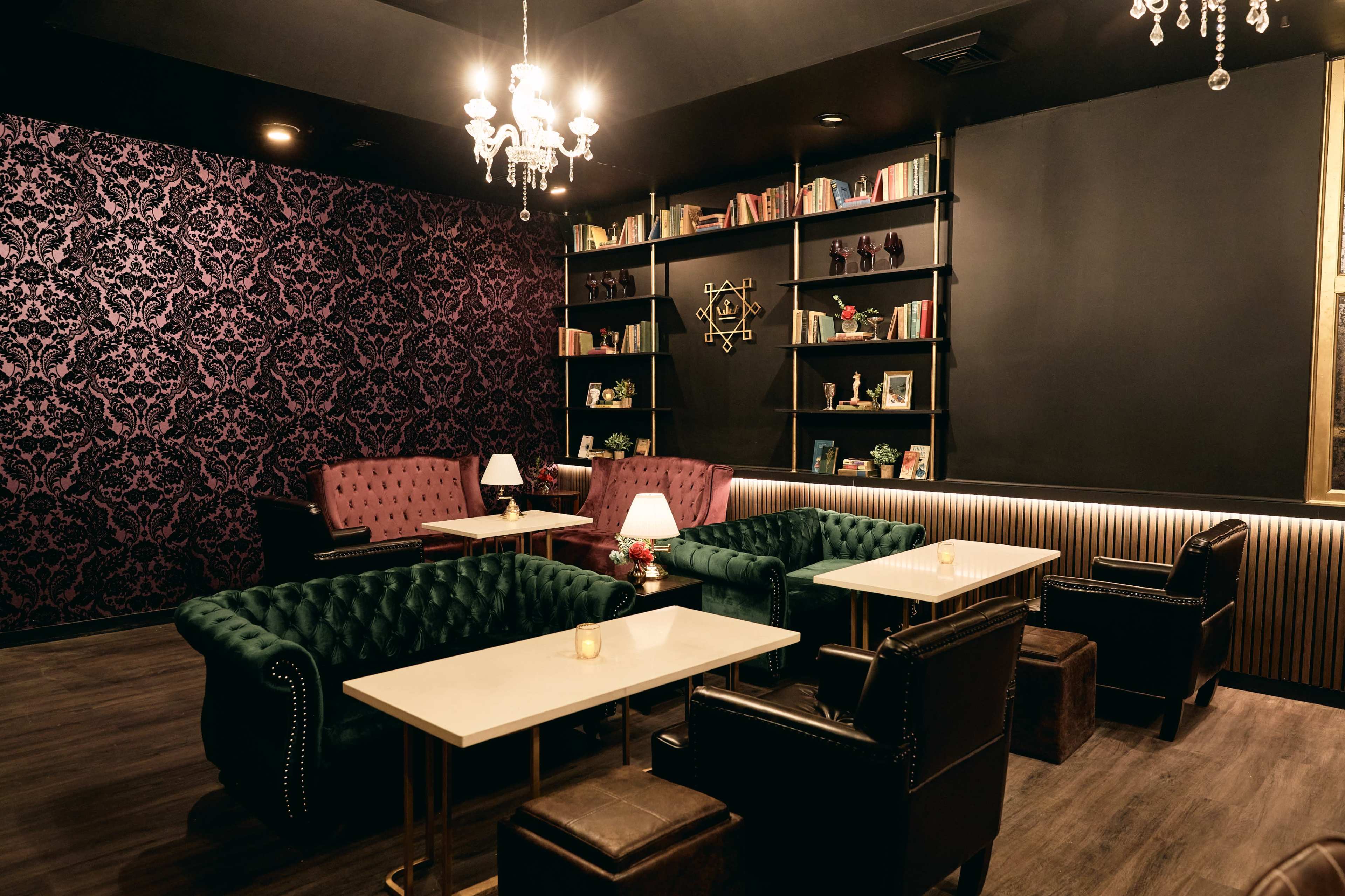 A stylish lounge area with velvet seating, bookshelves, and a chandelier in a dimly lit space.