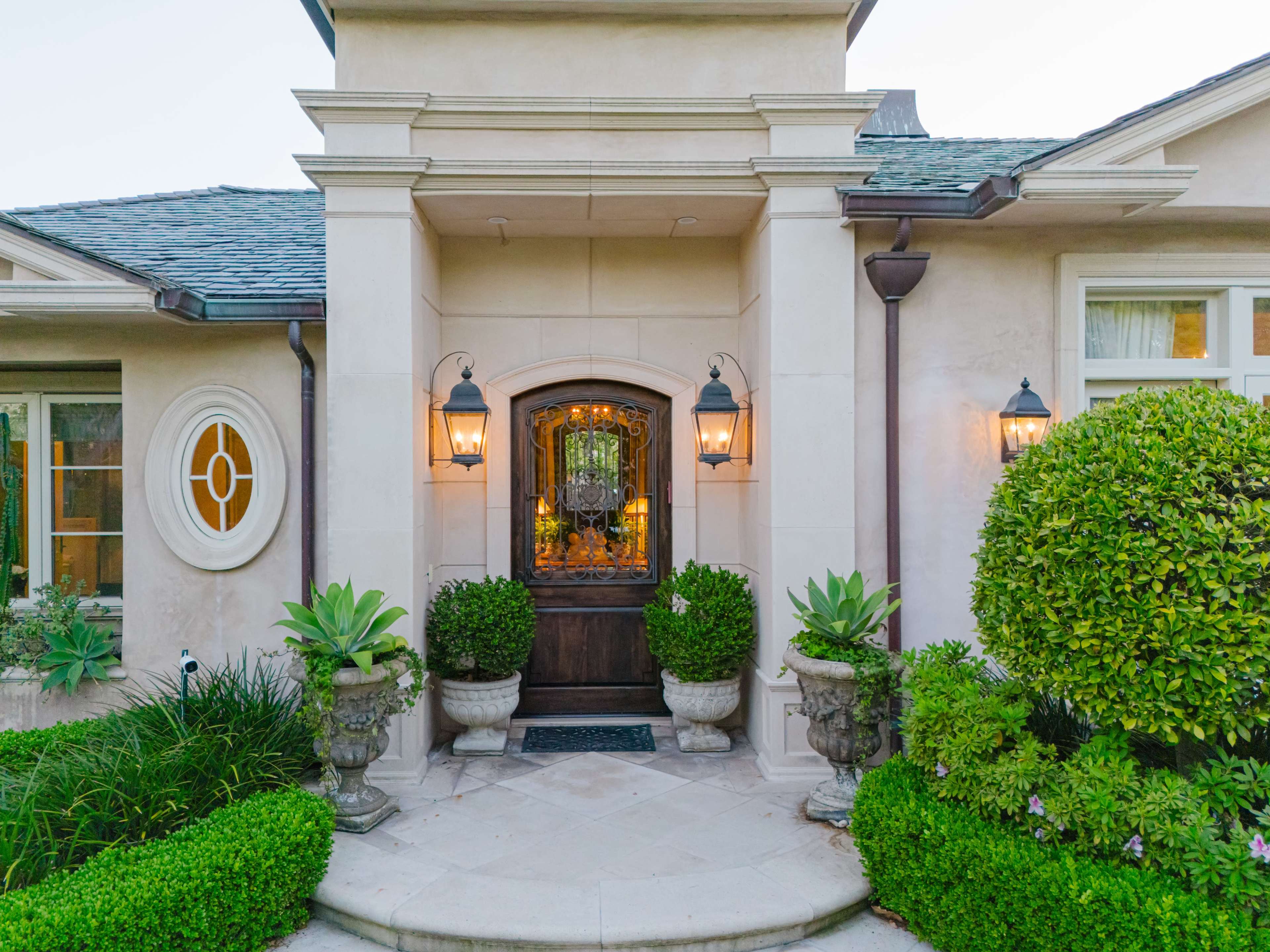 A welcoming front entrance of a house with decorative lanterns, potted plants, and a prominent wooden door.