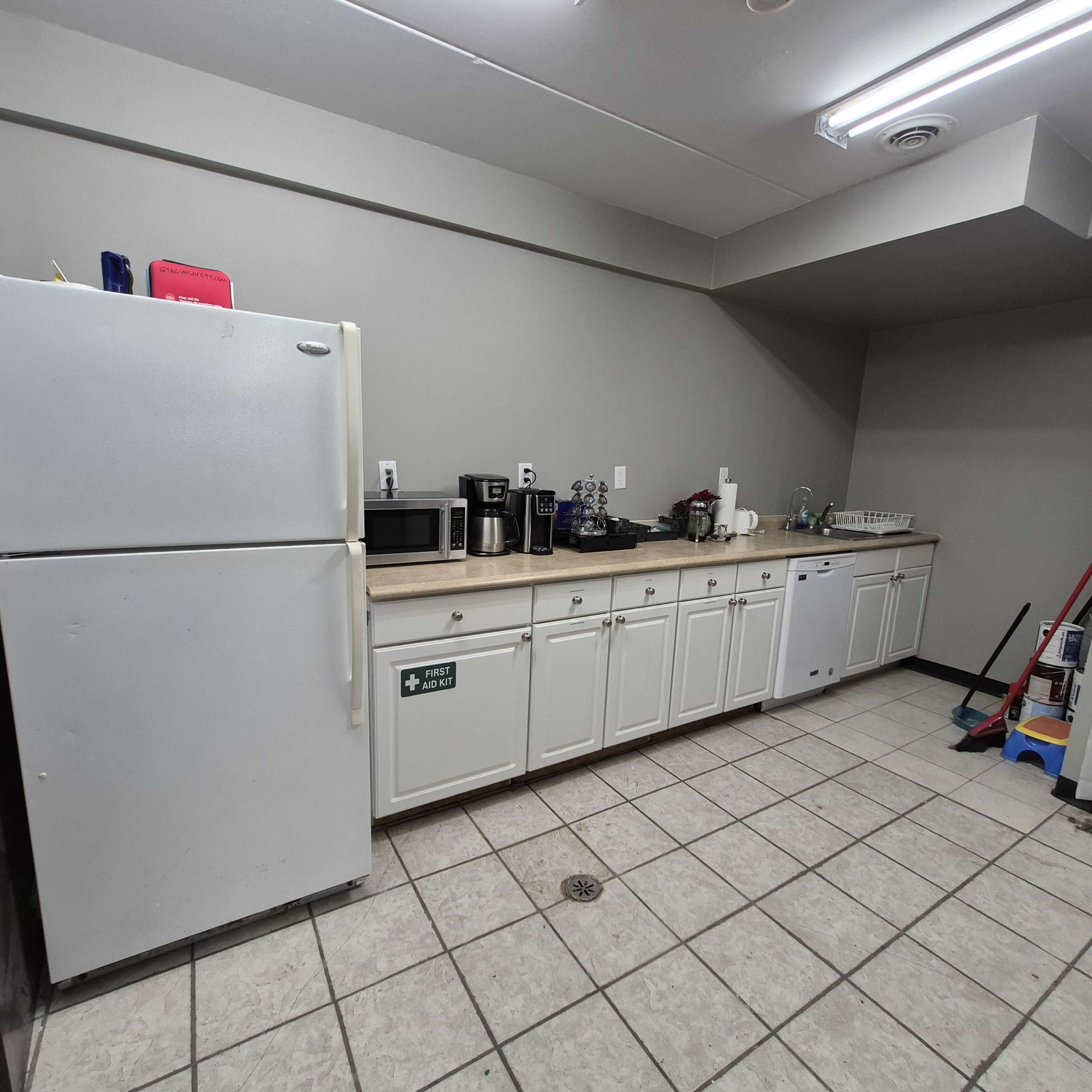 The image shows a kitchen with a refrigerator, microwave, coffee maker, and a sink along a tiled countertop.