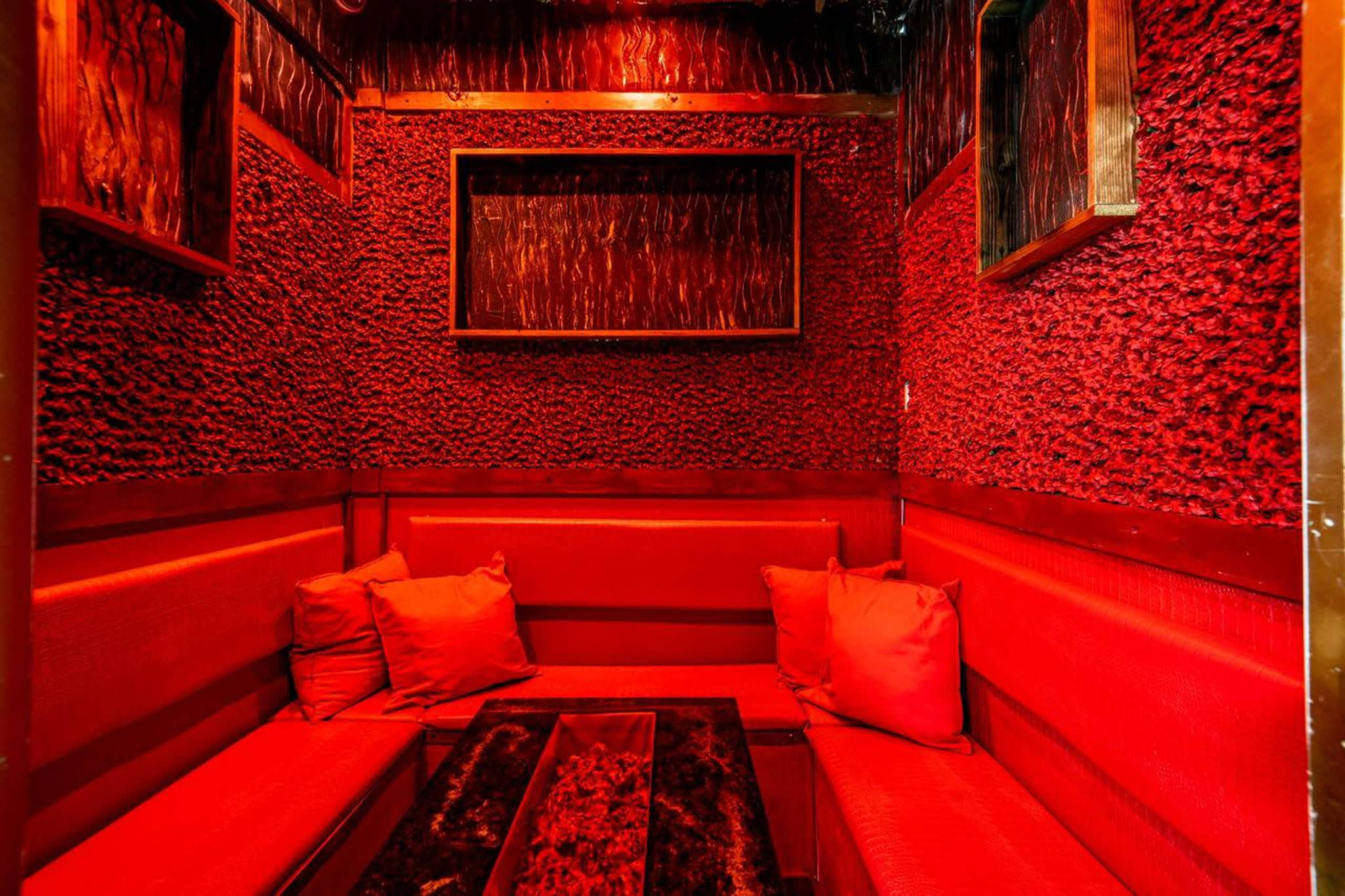 The image shows a small seating area with red textured walls, red cushions, and a dark table in the center.