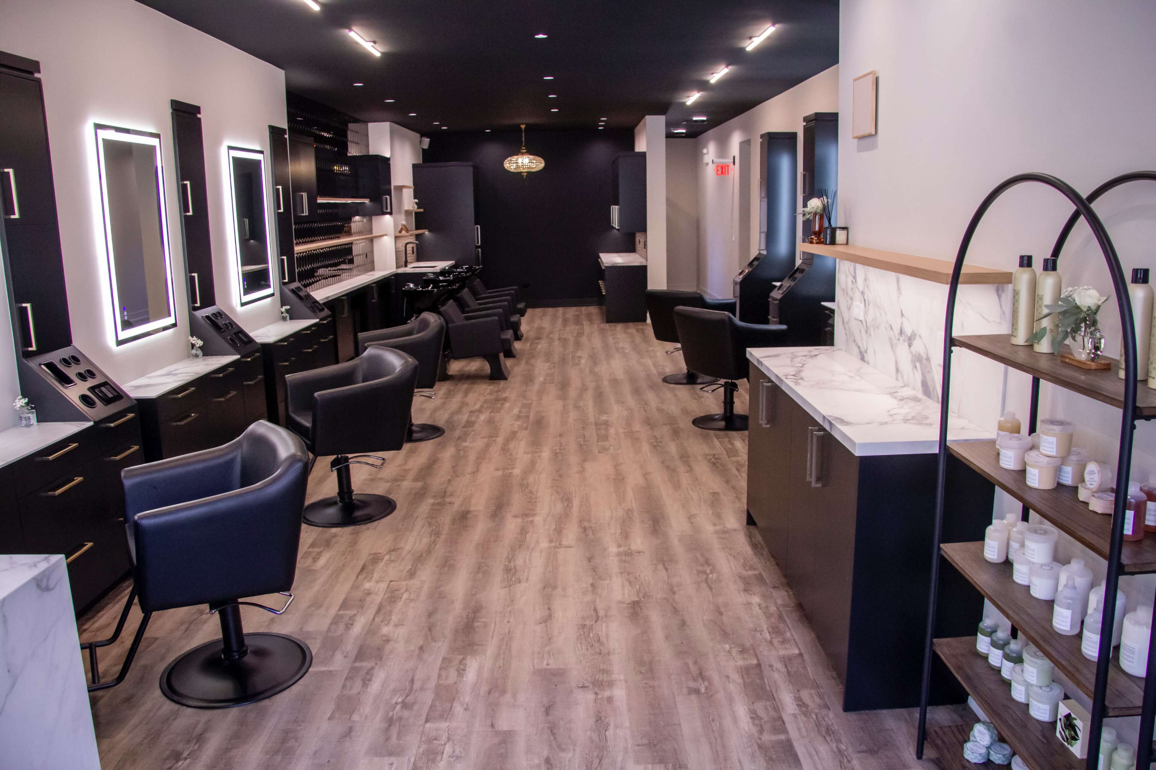 The image shows a modern salon interior with sleek black chairs, marble-topped counters, and well-organized product displays along the wall.