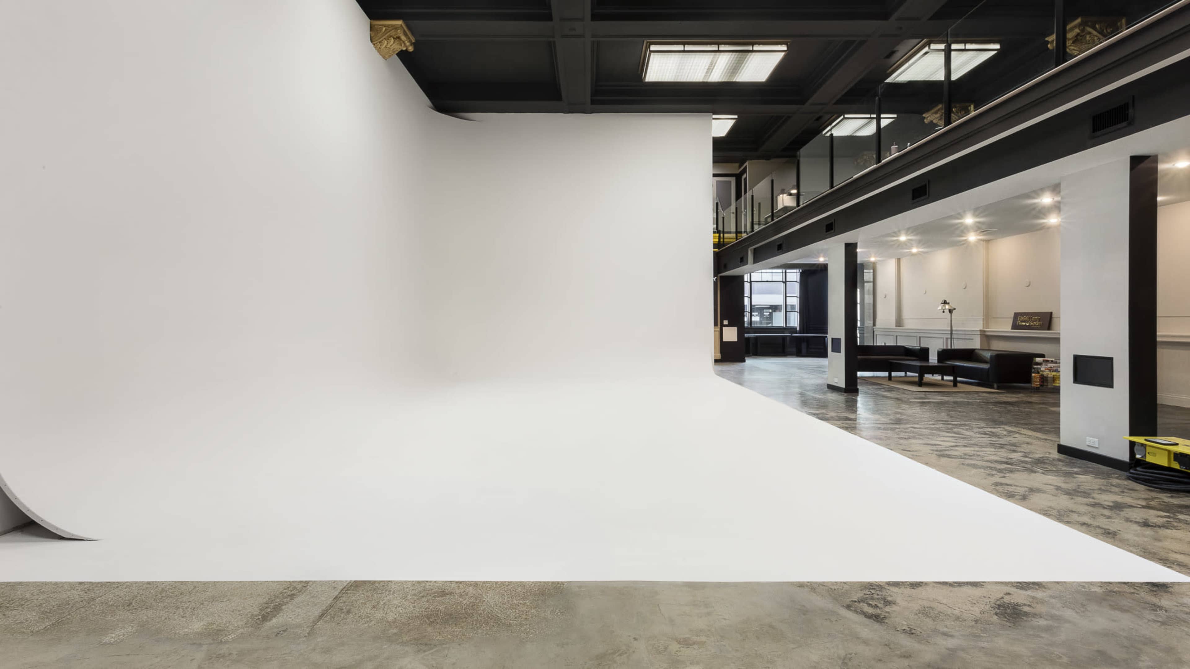 An empty studio space features a large white backdrop and a concrete floor, with a modern design and industrial lighting.